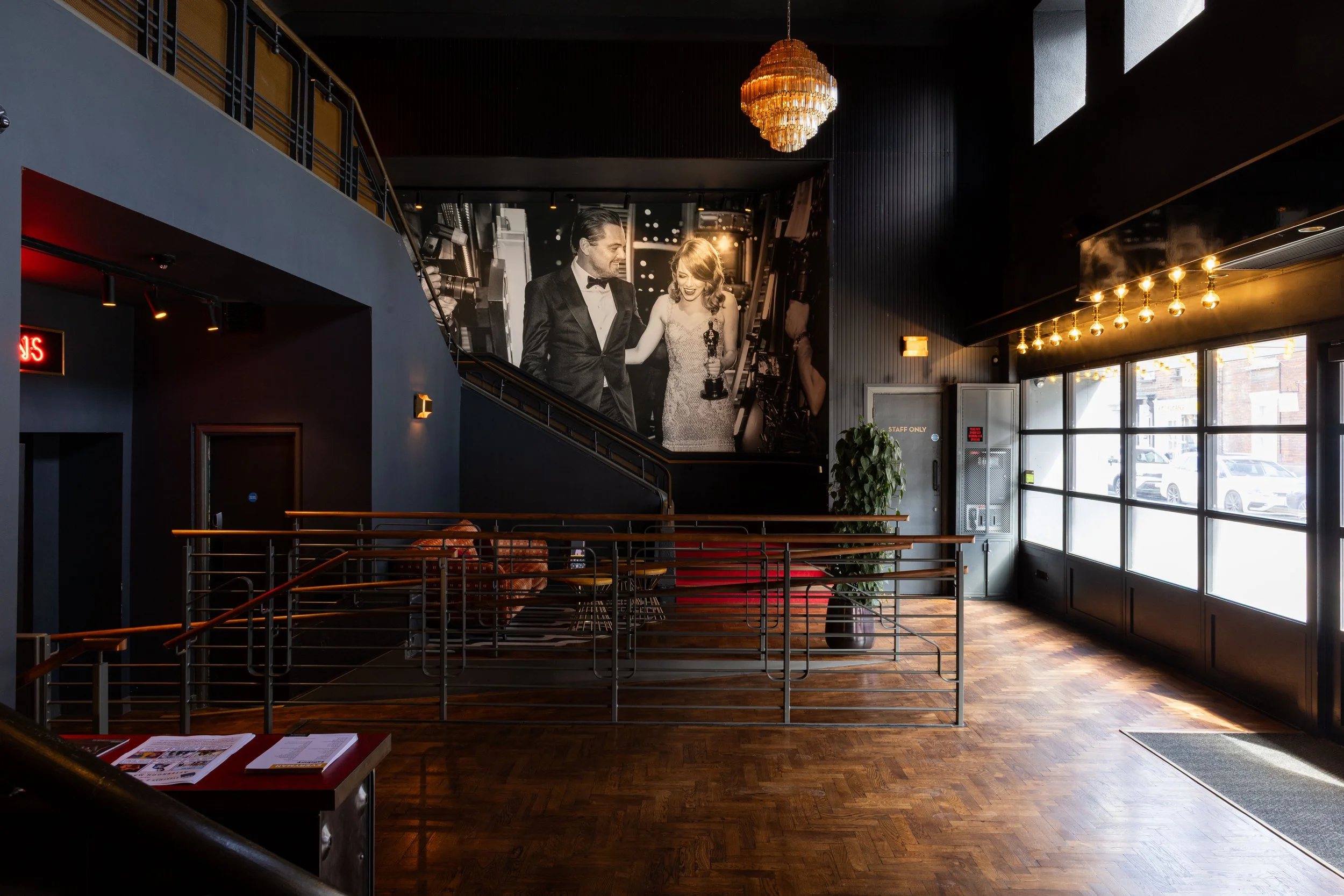 Interior of a modern venue with a large black-and-white photo of a man and woman in formal attire, chandeliers, large windows, and wooden floors.