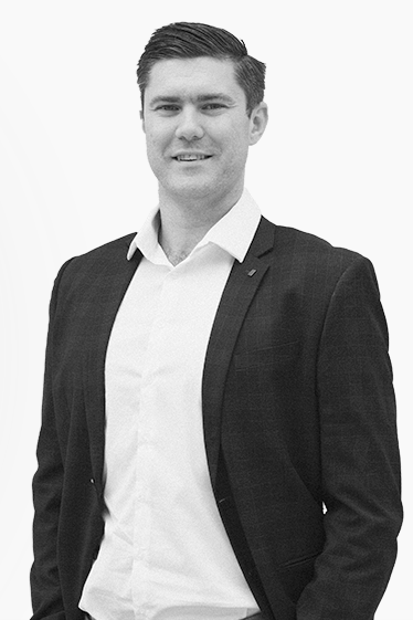 Black and white photo of a man in a suit and white shirt, smiling at the camera.