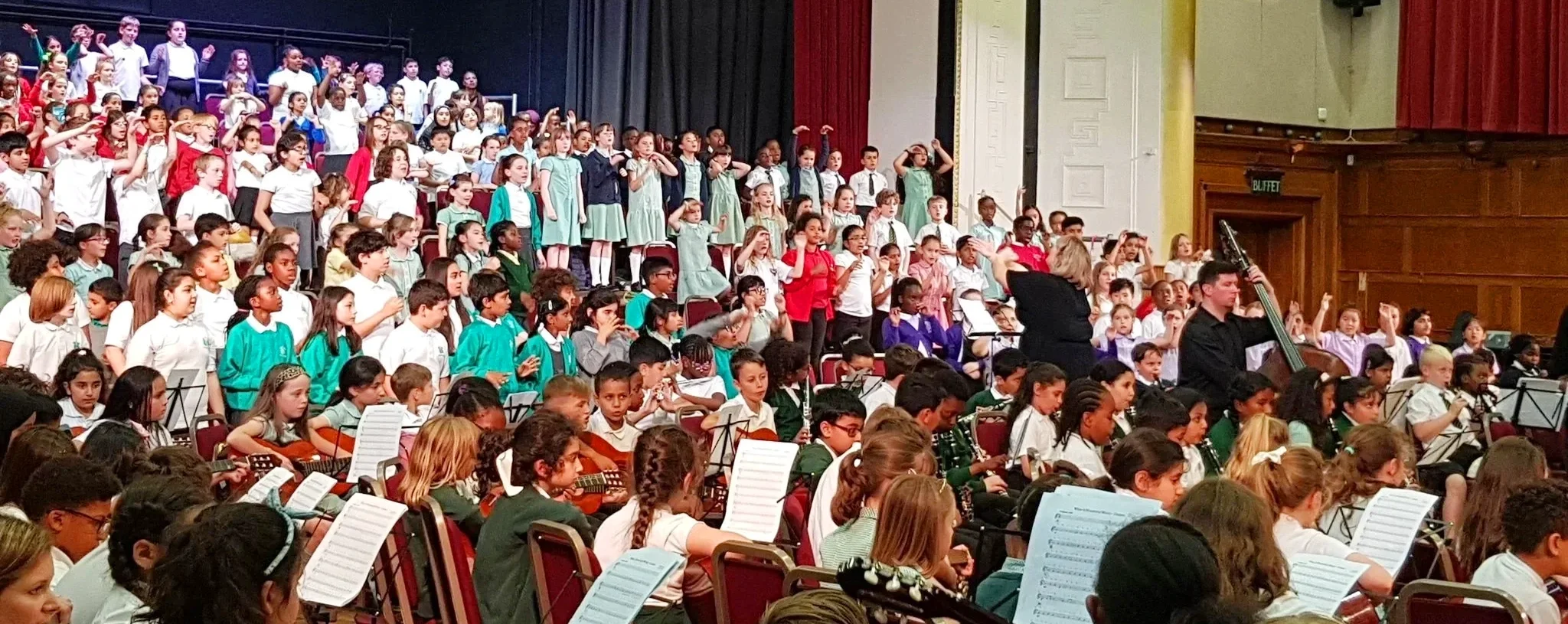 A very large ensemble of children on stage at Waltham Forest Assembly Hall in London, UK in an East London Music Group education project