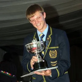 A young man in a formal blazer holding a trophy and smiling.