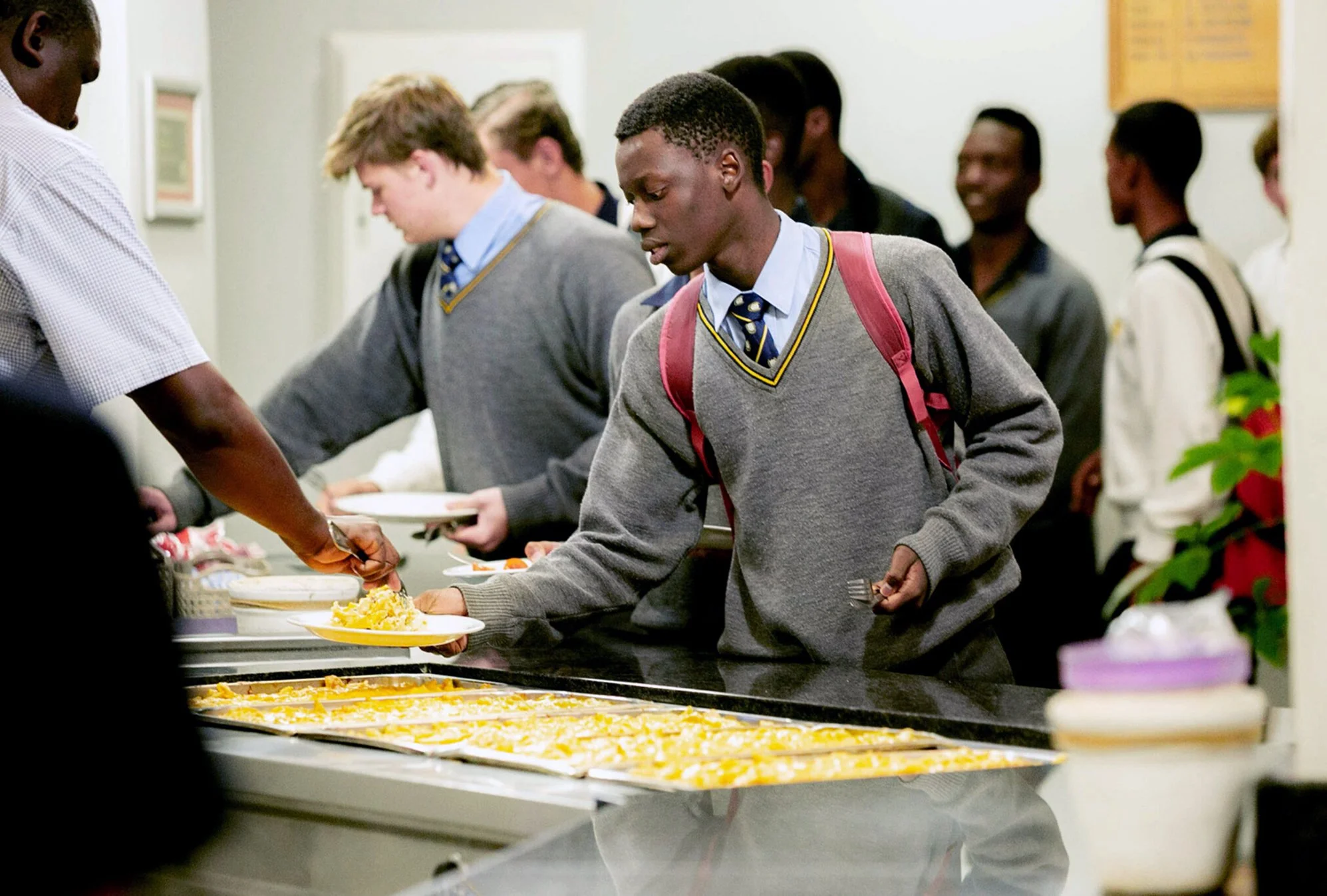 Students in school uniforms serving themselves food at a cafeteria buffet.
