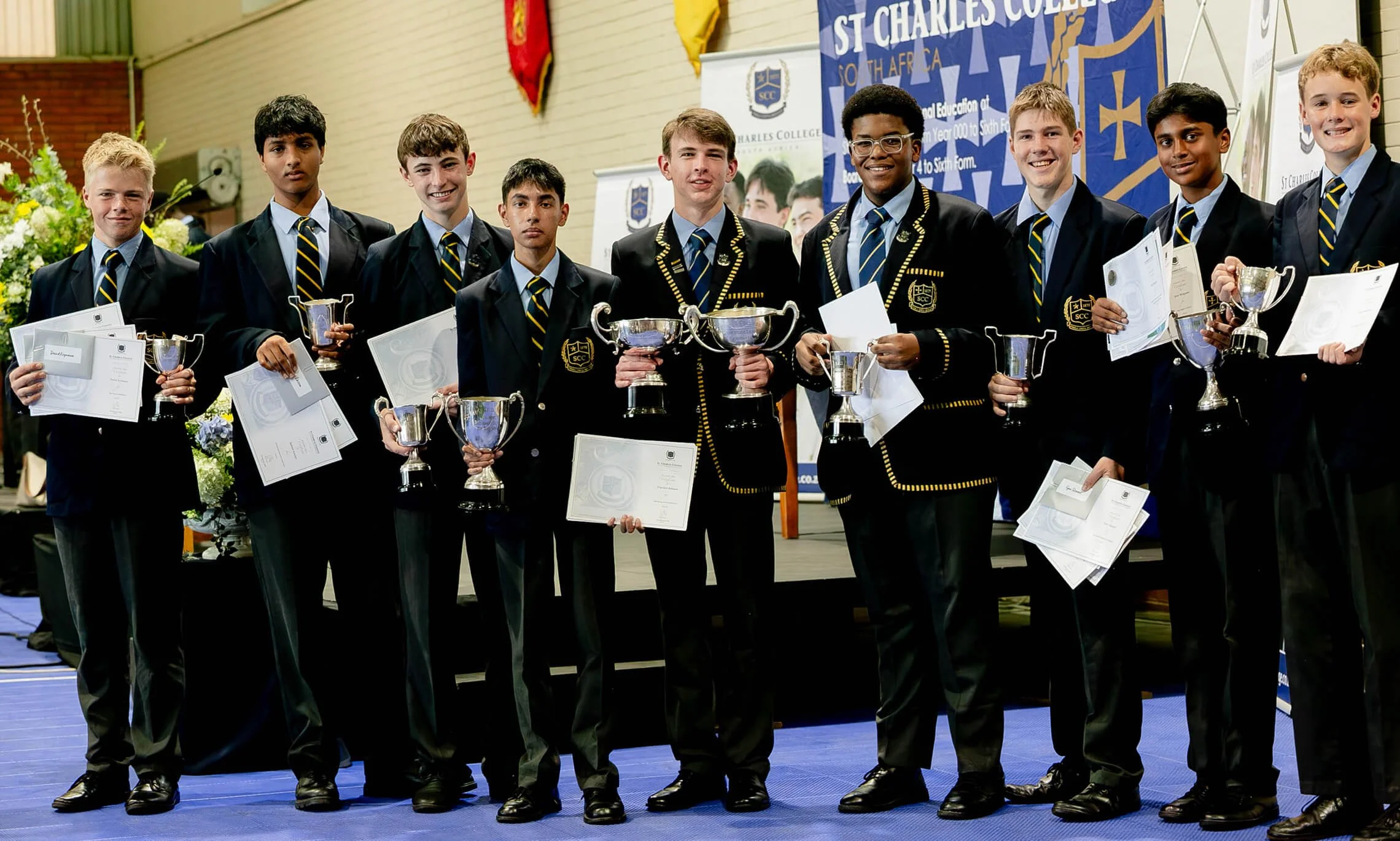 A group of young boys dressed in school uniforms holding trophies and certificates at an award ceremony.