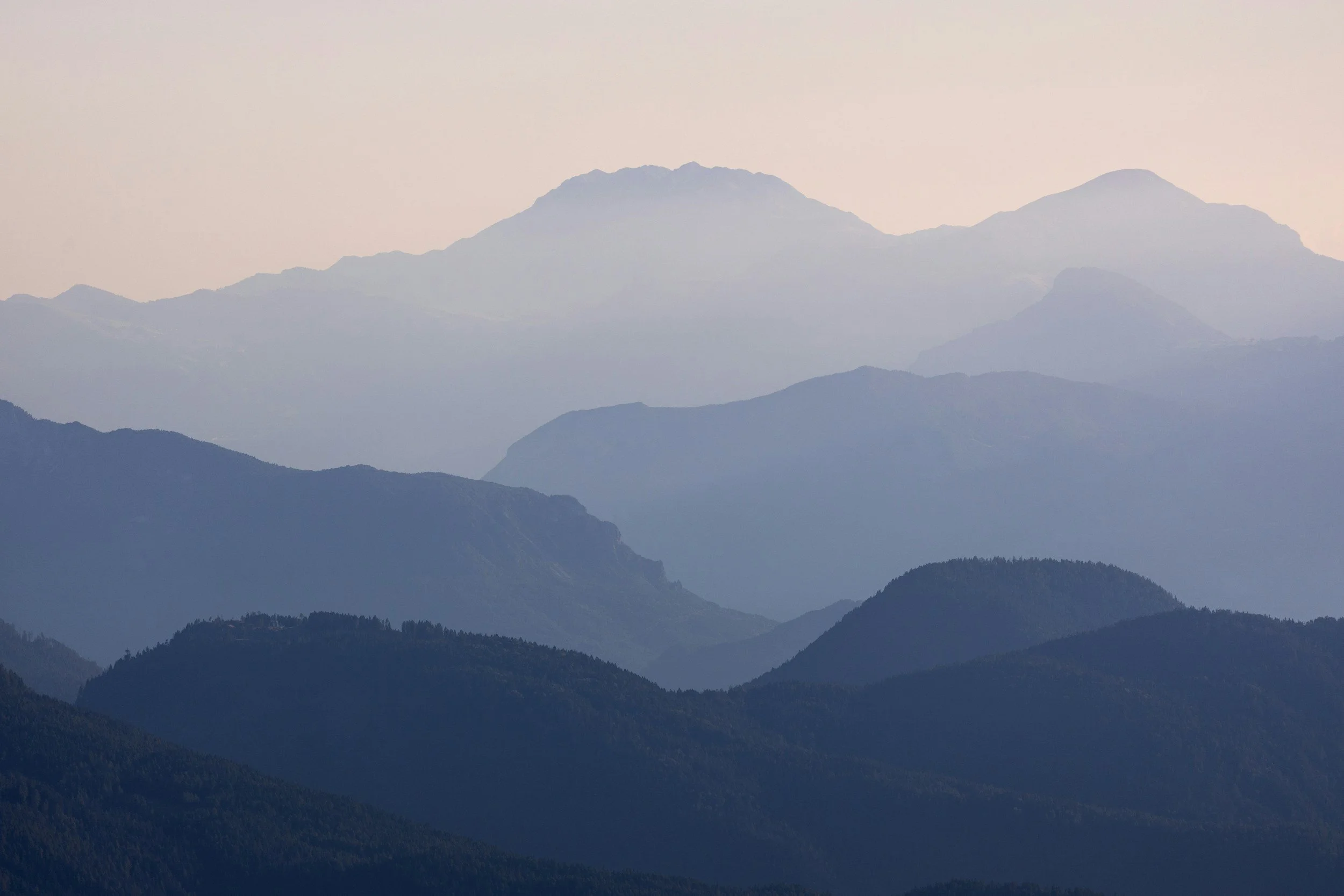 A landscape of layered mountains or hills with a soft, pastel sky in the background.