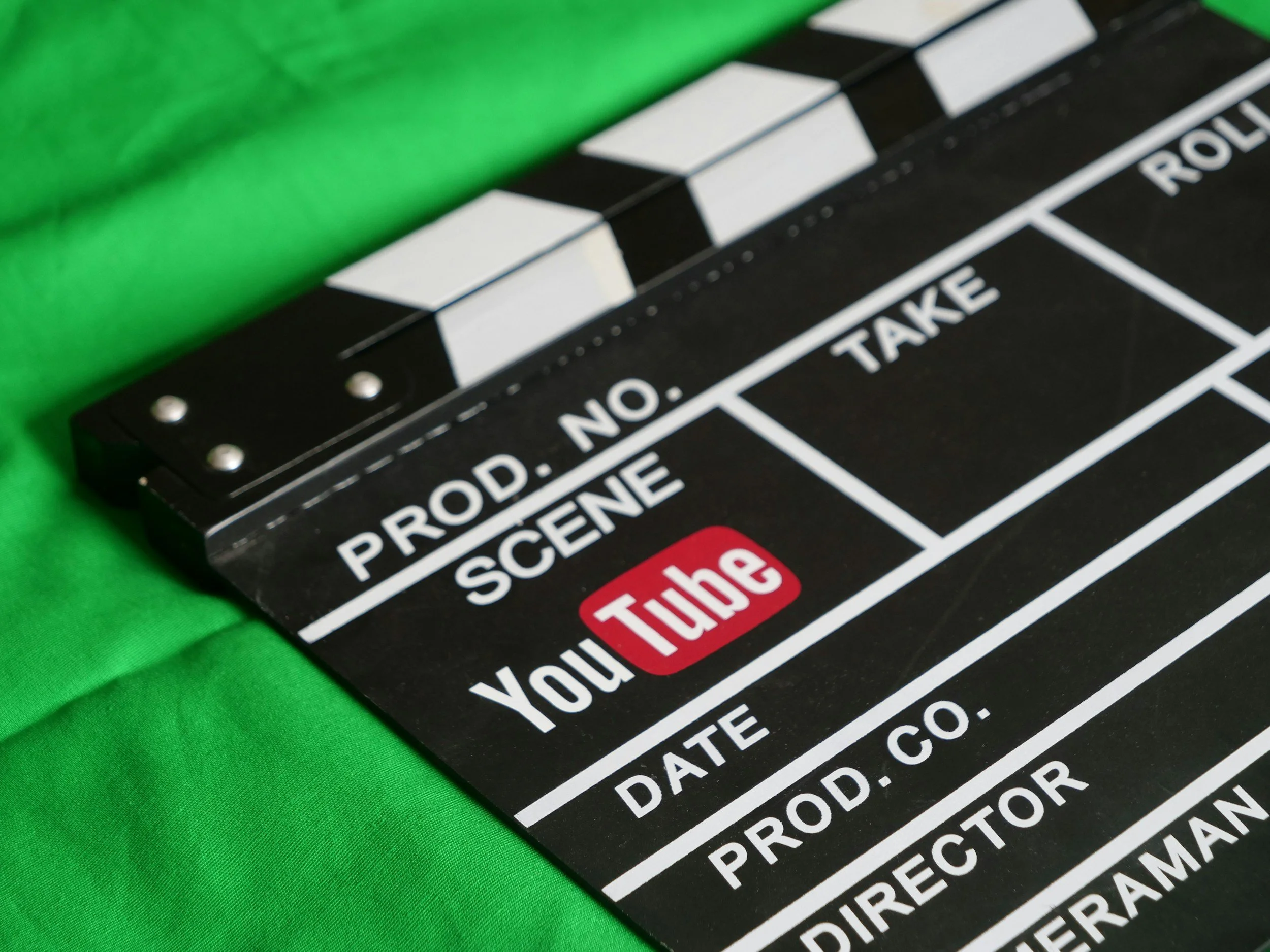 Close-up of a black and white clapperboard with text for scene, take, and director, resting on a green fabric background.