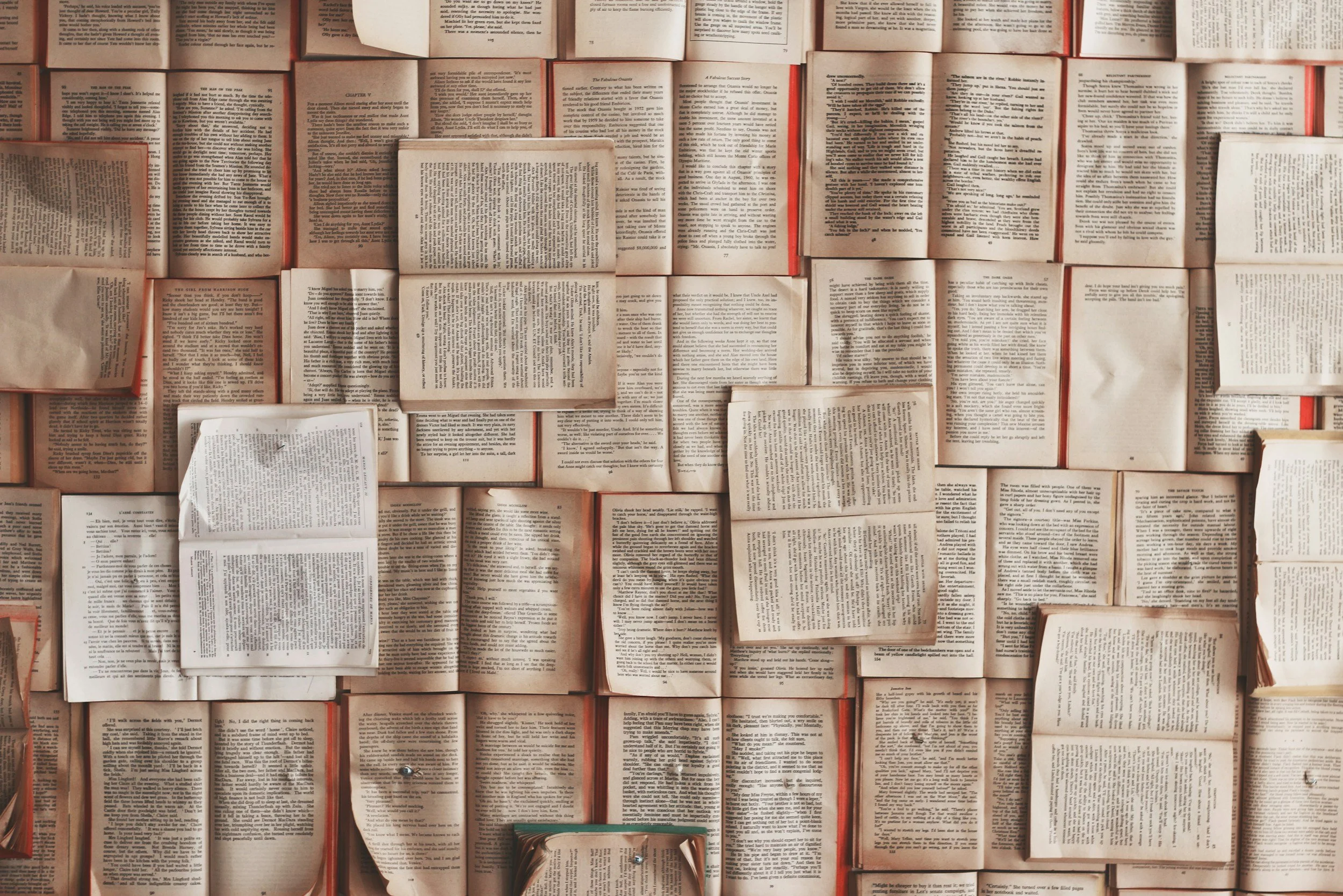 A collection of open books spread out on a surface, with some stacked on top of each other and pages visible.