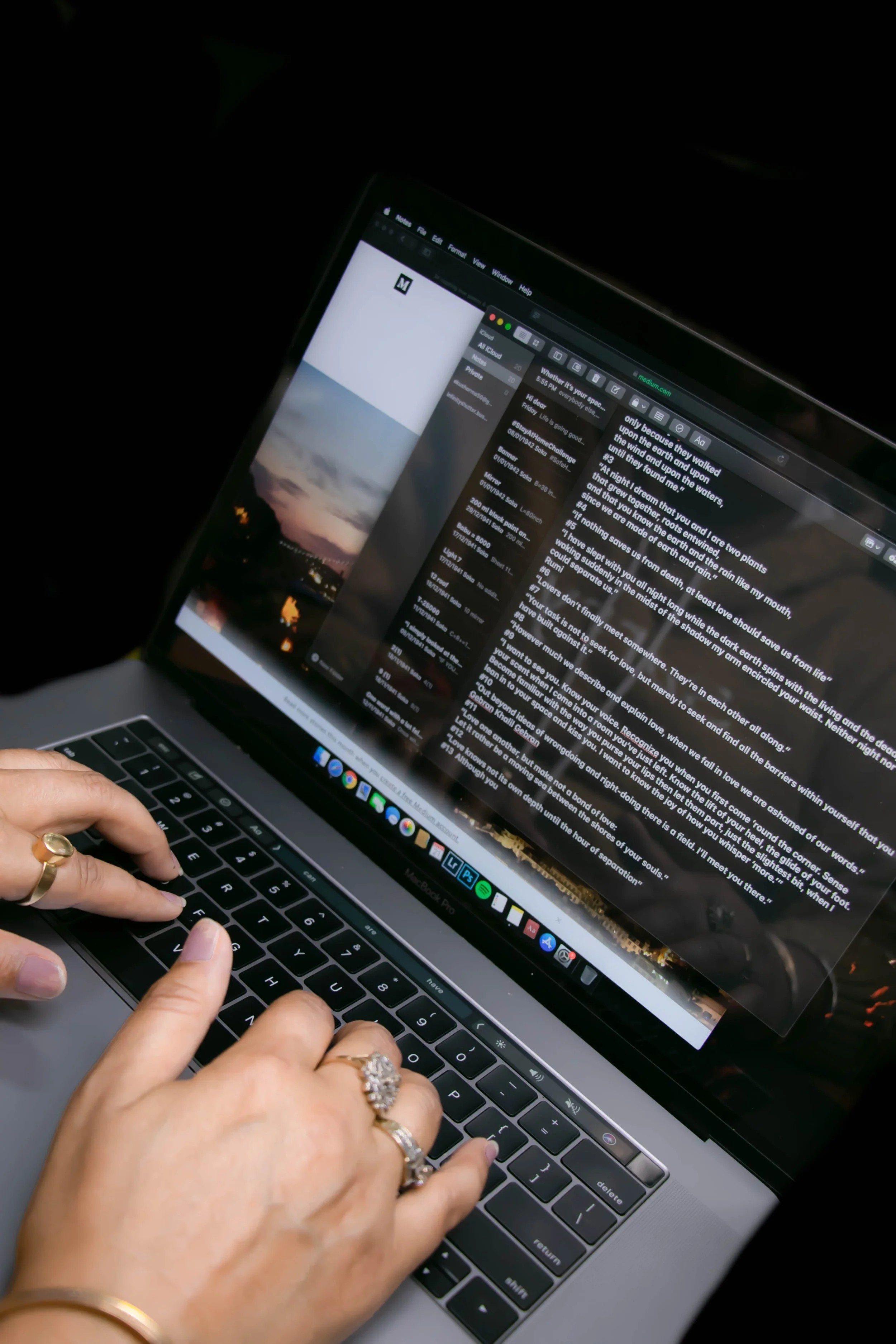 Close-up of a person's hands typing on a MacBook keyboard, with a photo of a sunset and sky on the screen, and multiple open tabs and email messages visible.