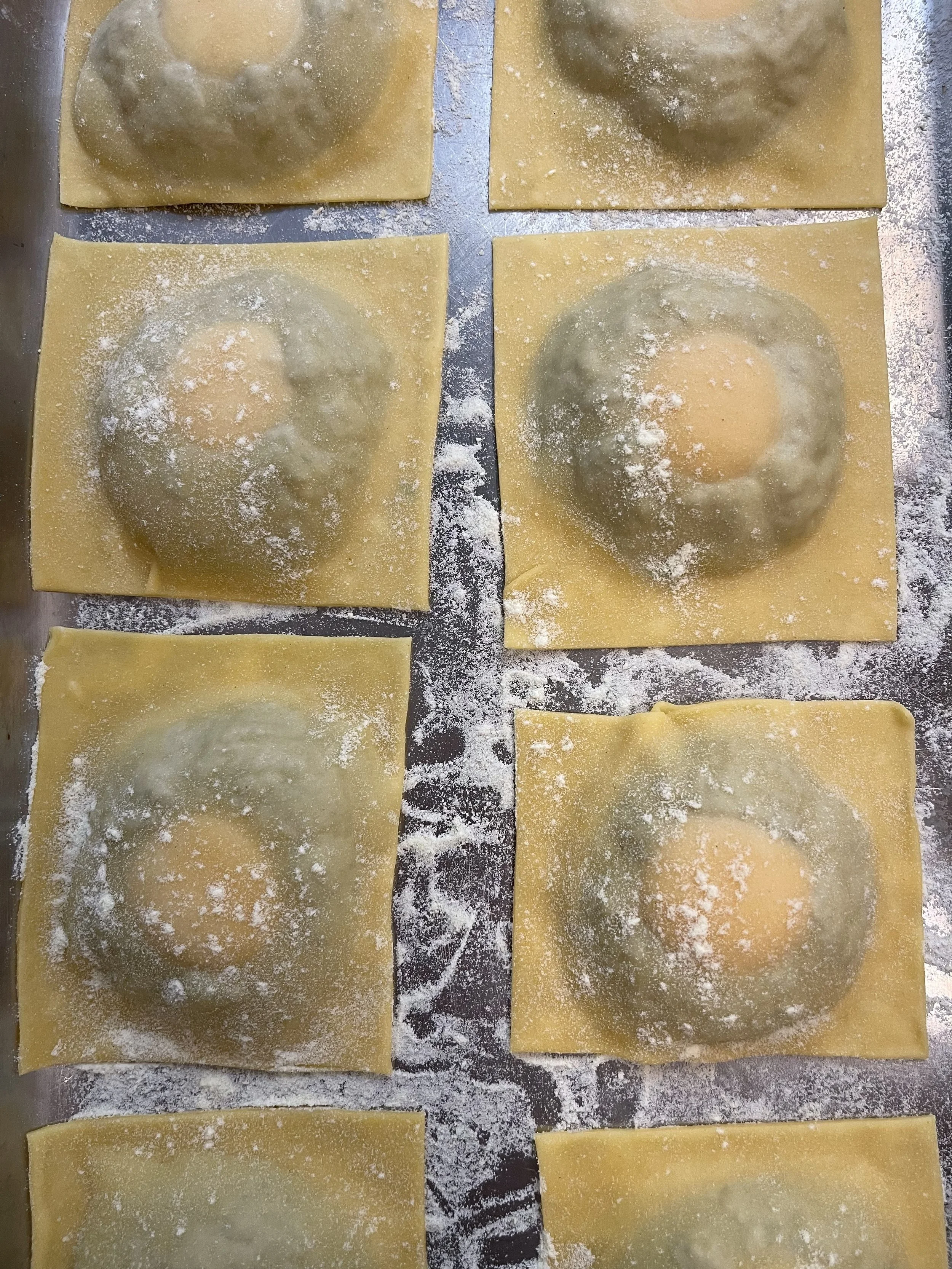 Four squares of pasta dough with a centered round cutout, dusted with flour.