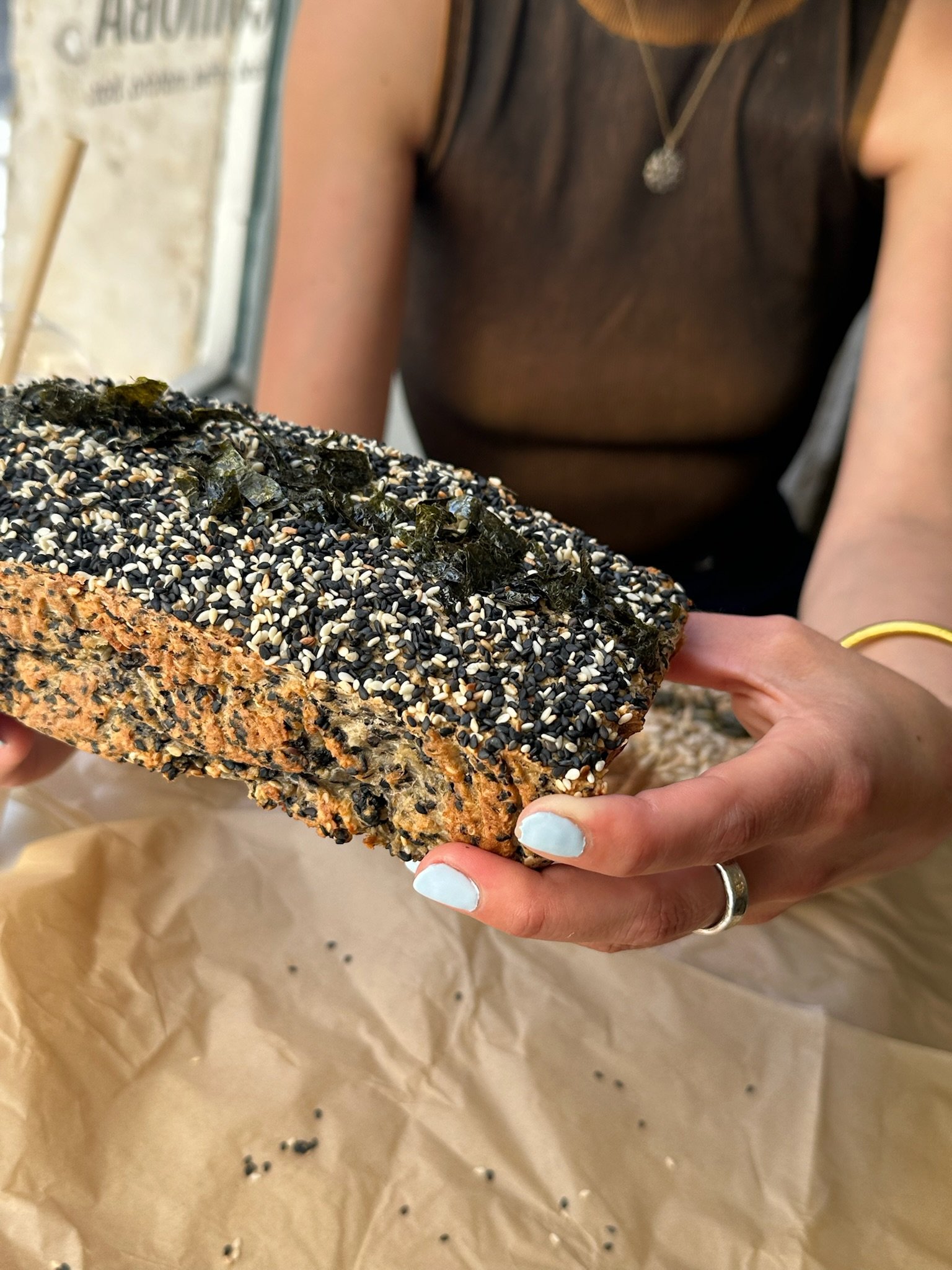 Person holding a piece of bread topped with seaweed and black and white sesame seeds.