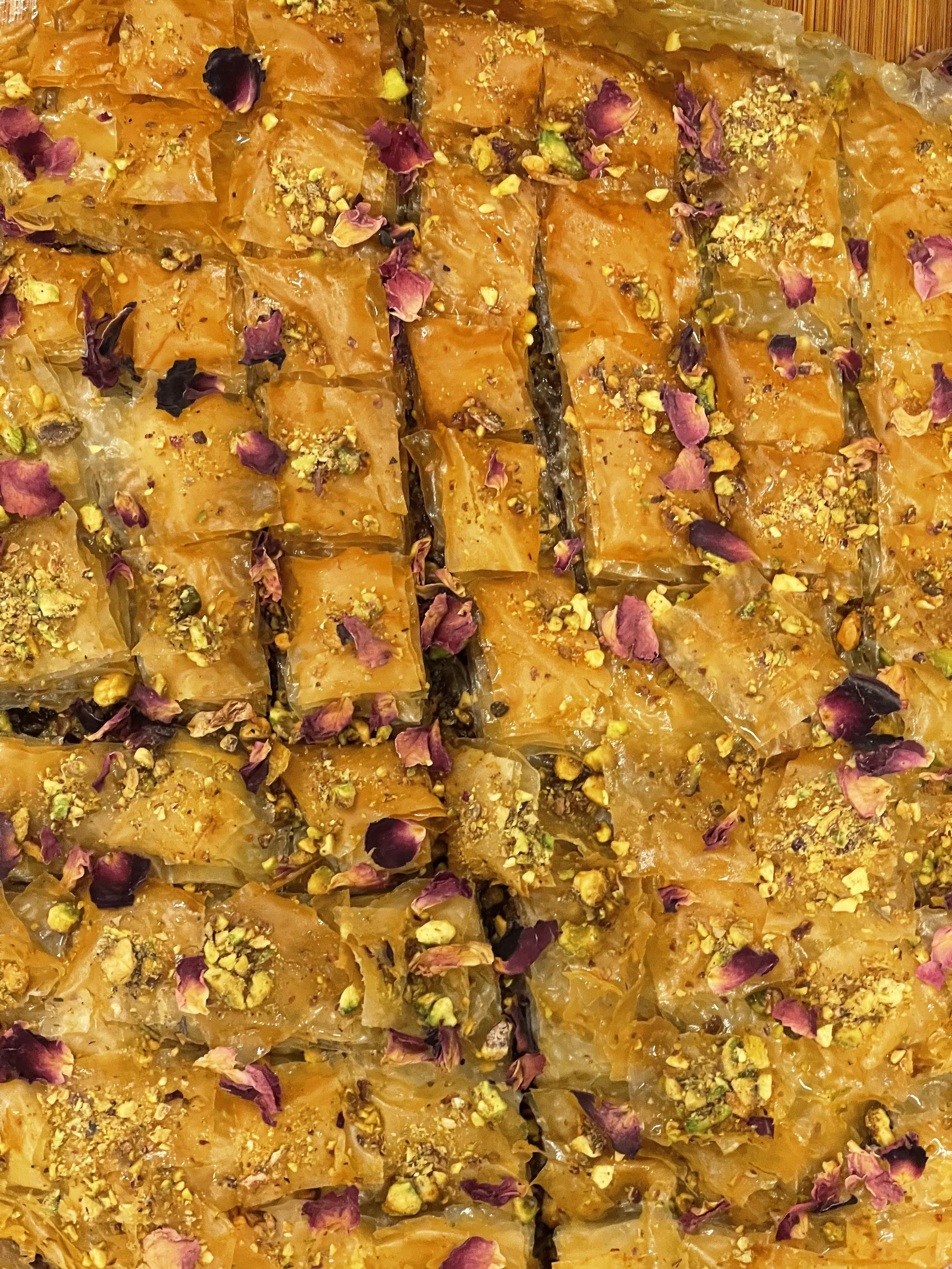 Close-up of multiple pieces of baklava topped with chopped pistachios and rose petals.