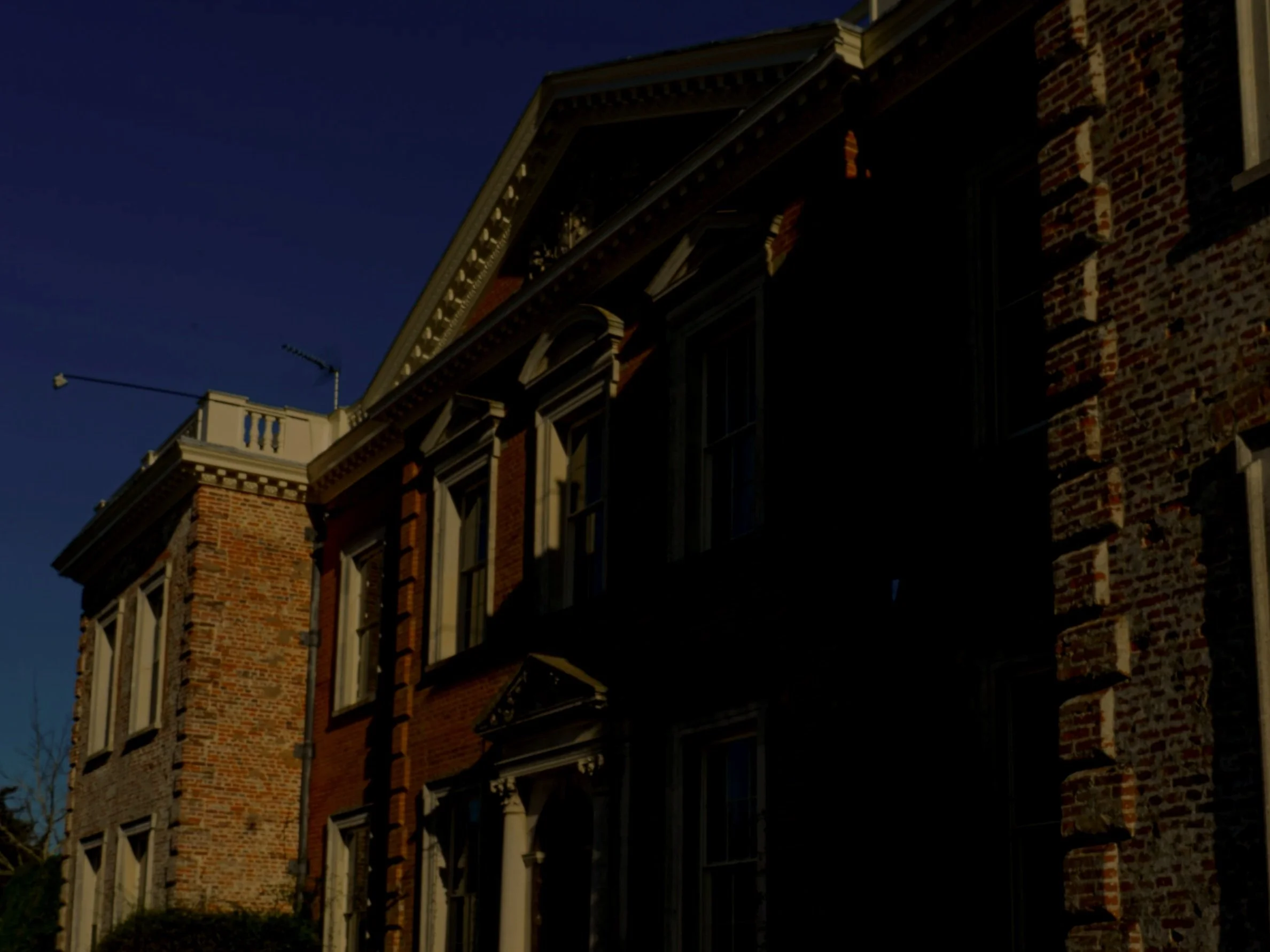 A historic brick building with multiple stories, ornate window frames, and decorative architectural details, captured during low light conditions.