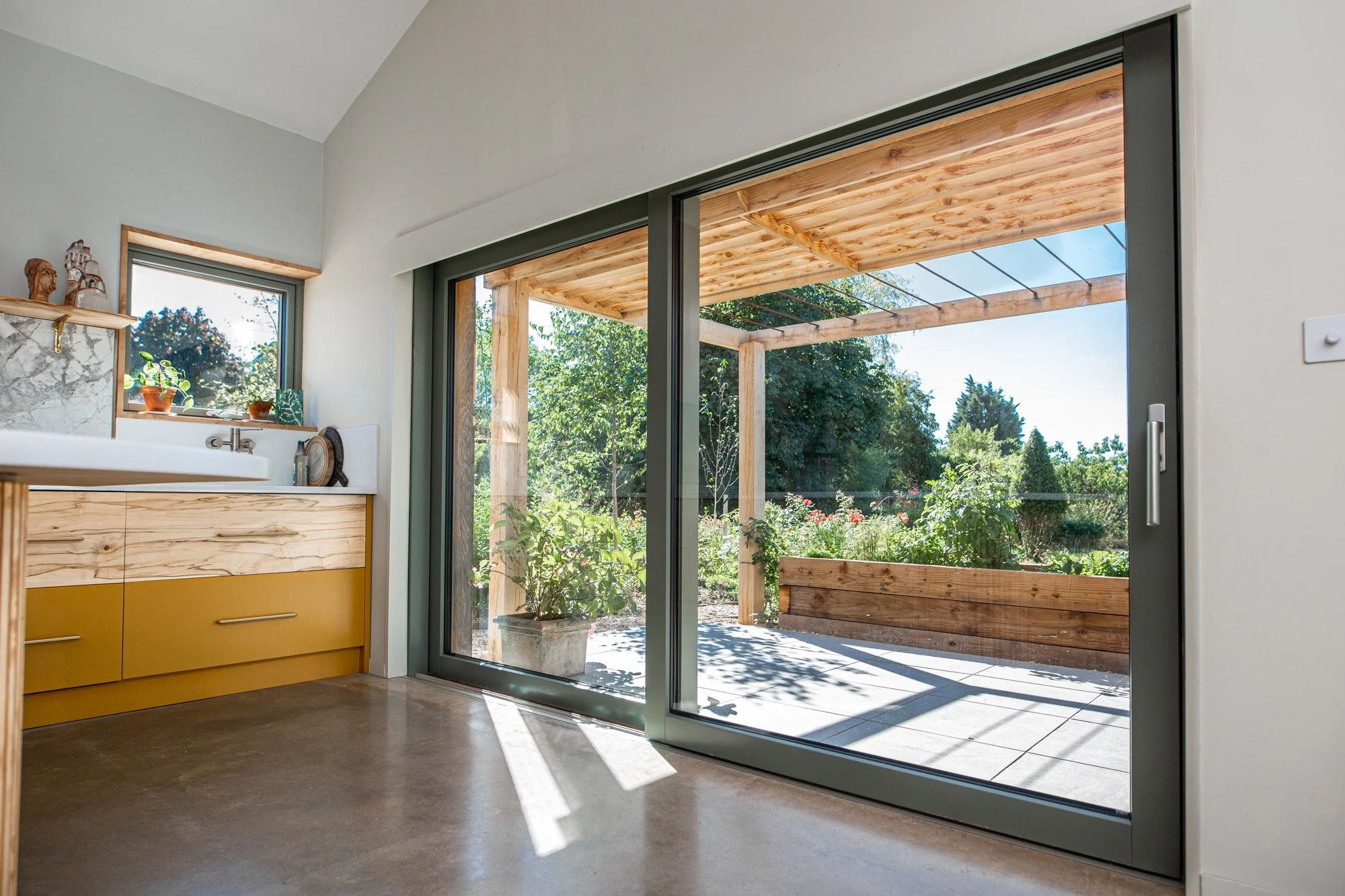 Interior view of a room with a large sliding glass door opening to a patio with wooden pergola and garden.