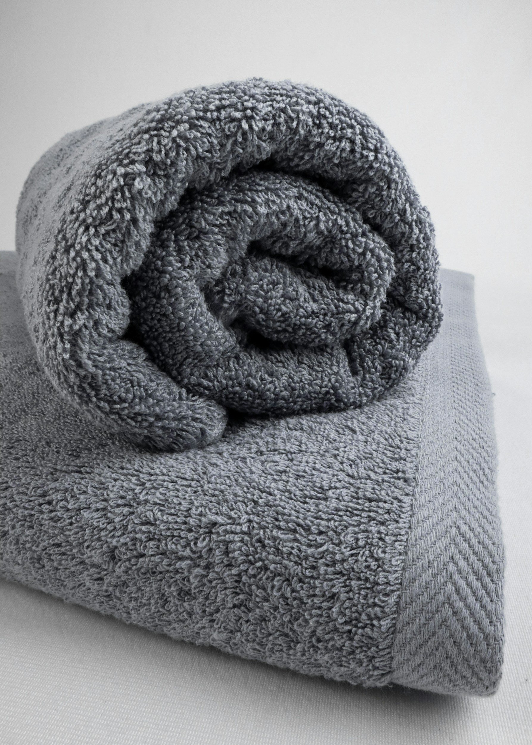 Rolled gray towel on a light gray fabric surface with a white plain background.