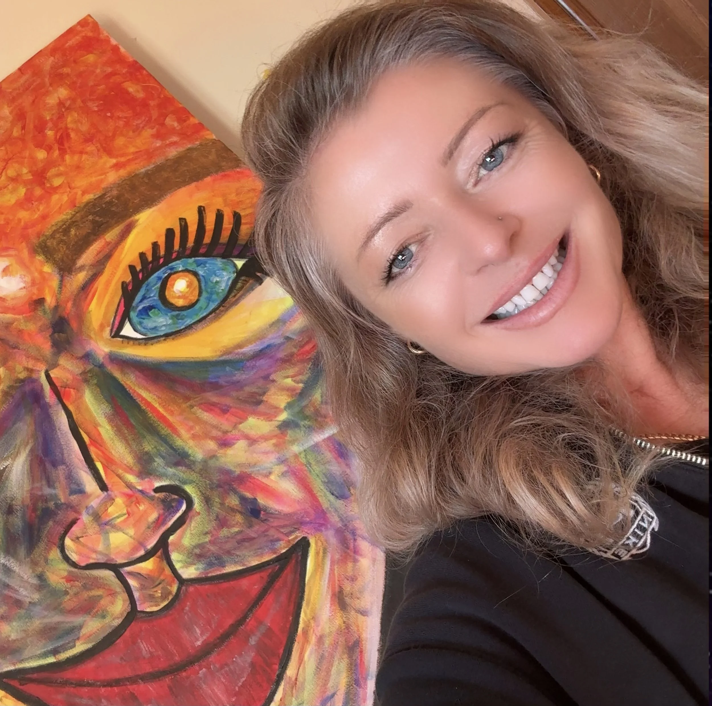Photograph of contemporary artist Nathaly Ellen Celia beside one of her colourful original paintings.