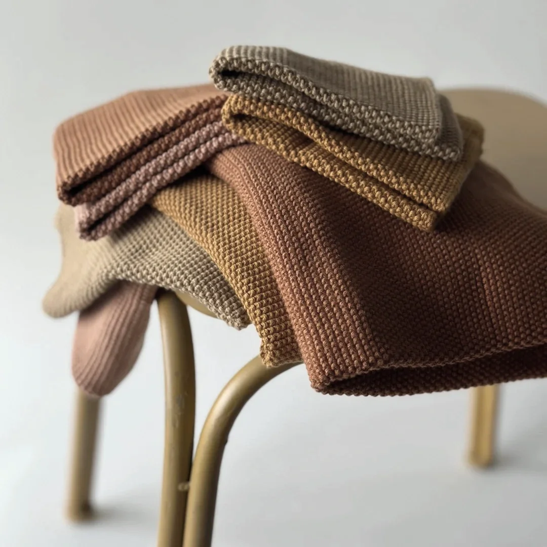Stack of folded clothes in various earthy tones on a beige stool.