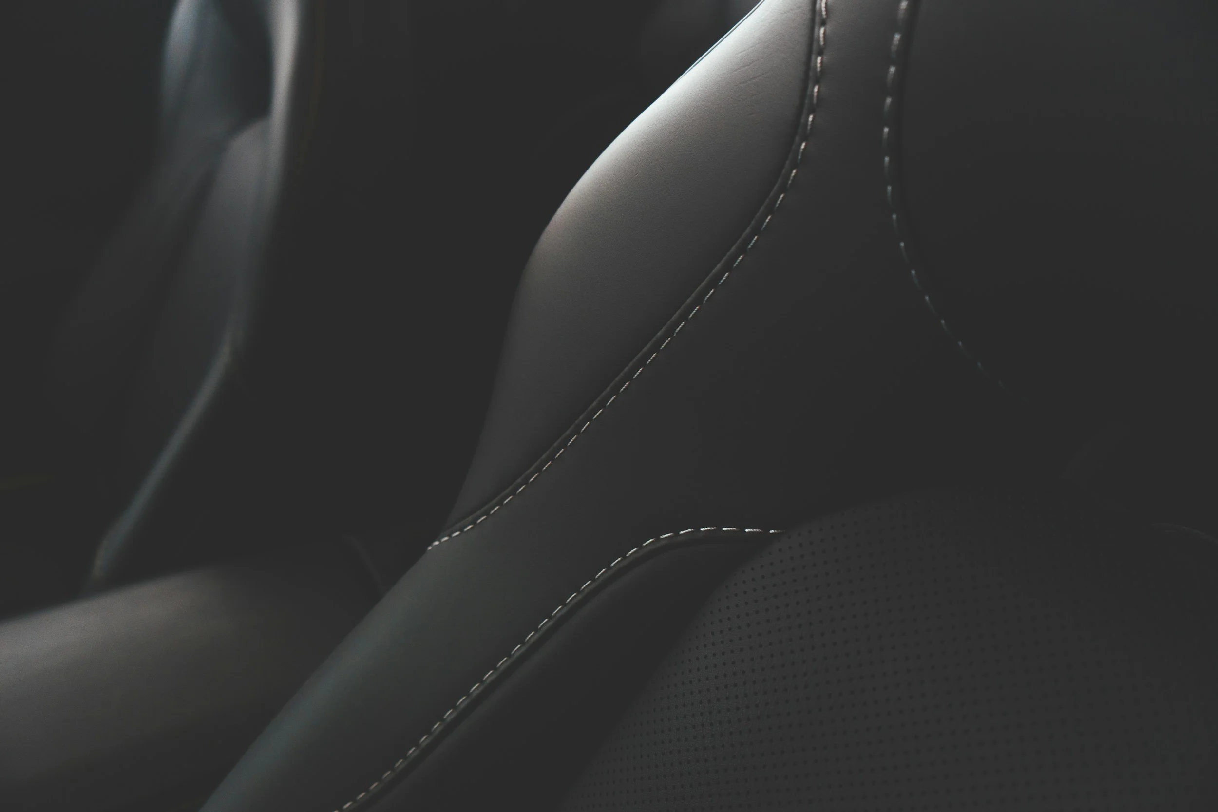 Close-up of black leather car seat with white stitching detail.