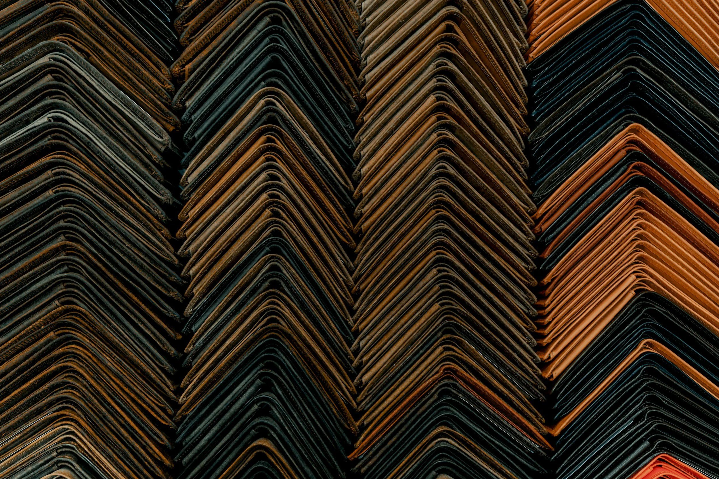 Stacked leather wallets in various shades of brown and black, arranged in a neat, overlapping pattern.