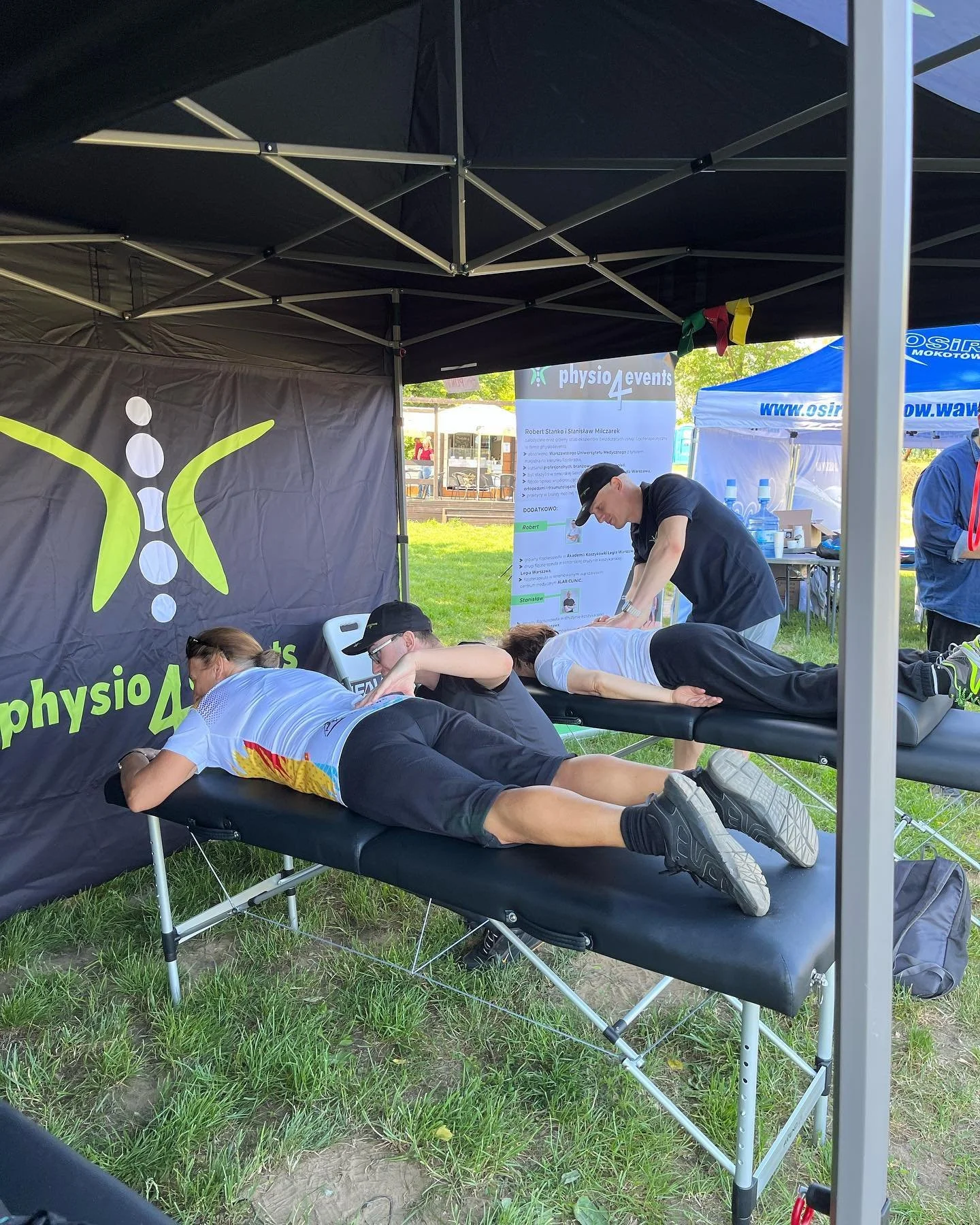 Two people receiving massages on portable massage tables at an outdoor event under a black tent.