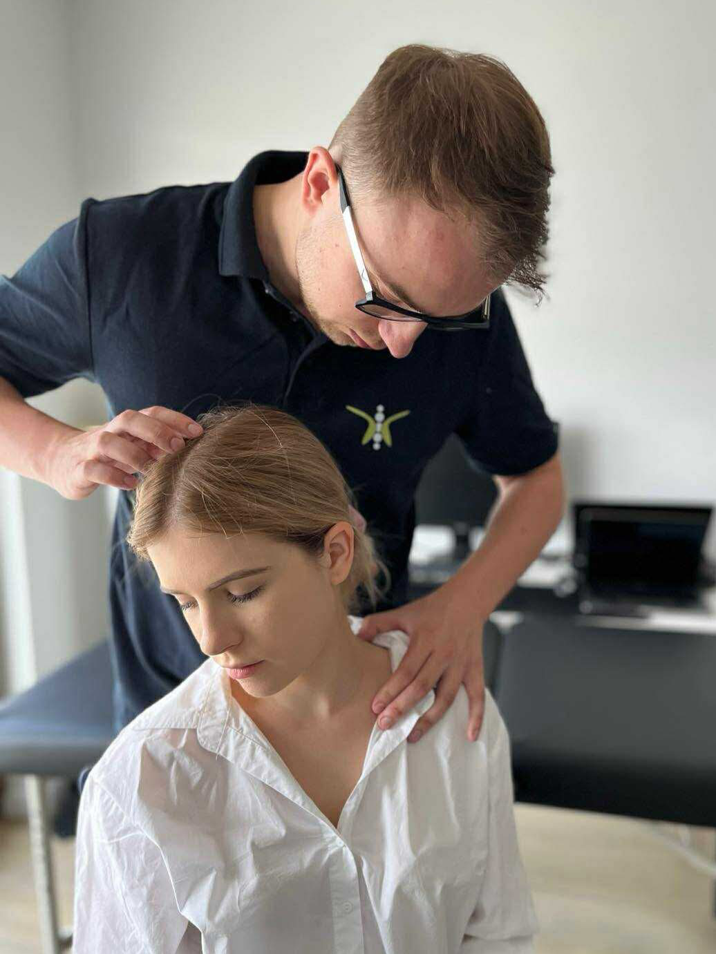 A chiropractor performs spinal adjustment on a woman sitting on an examination table.