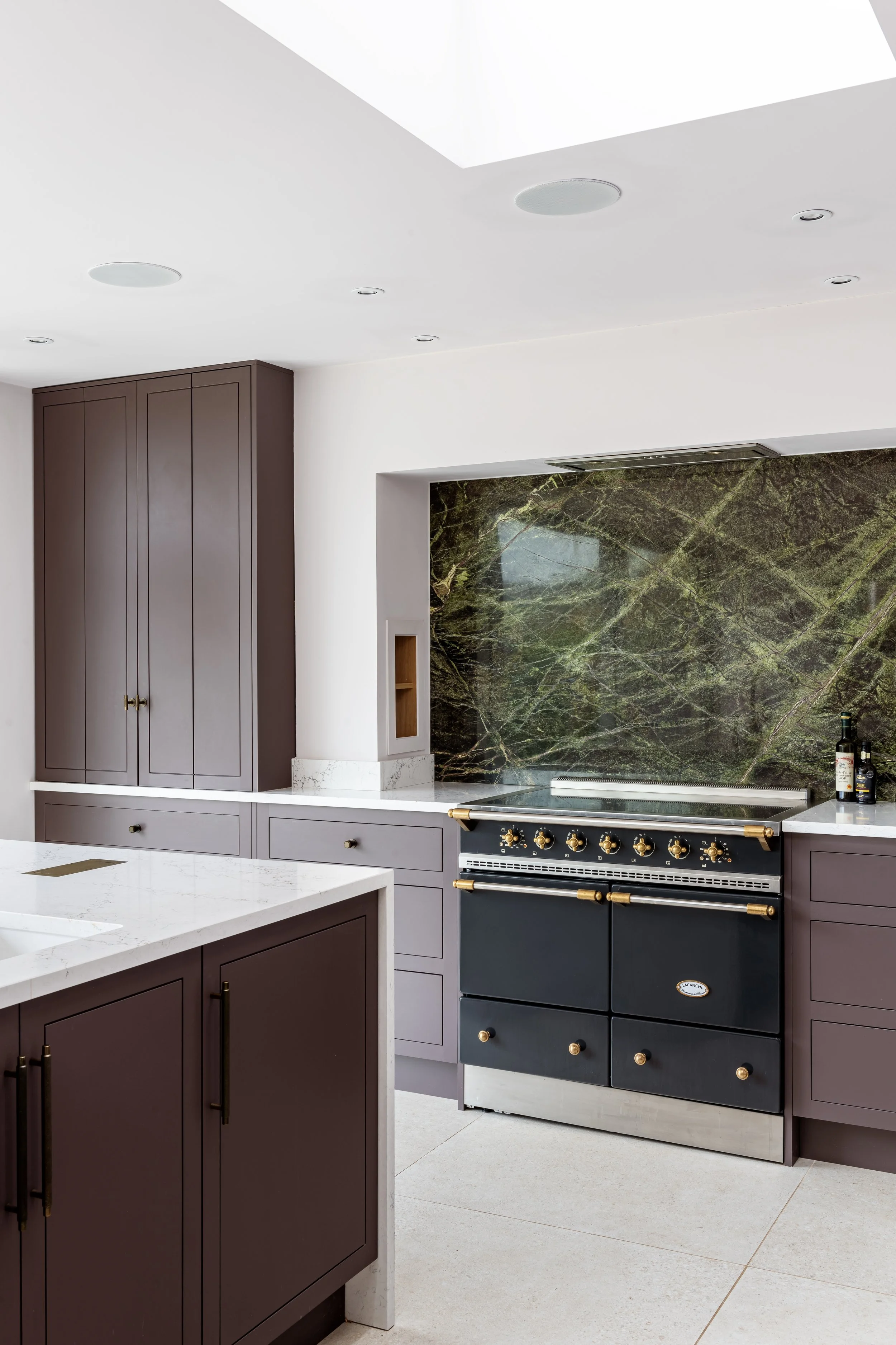 Modern kitchen by Gem Construction with purple cabinetry, marble countertops, a black stove with gold handles, and a green marble backsplash.