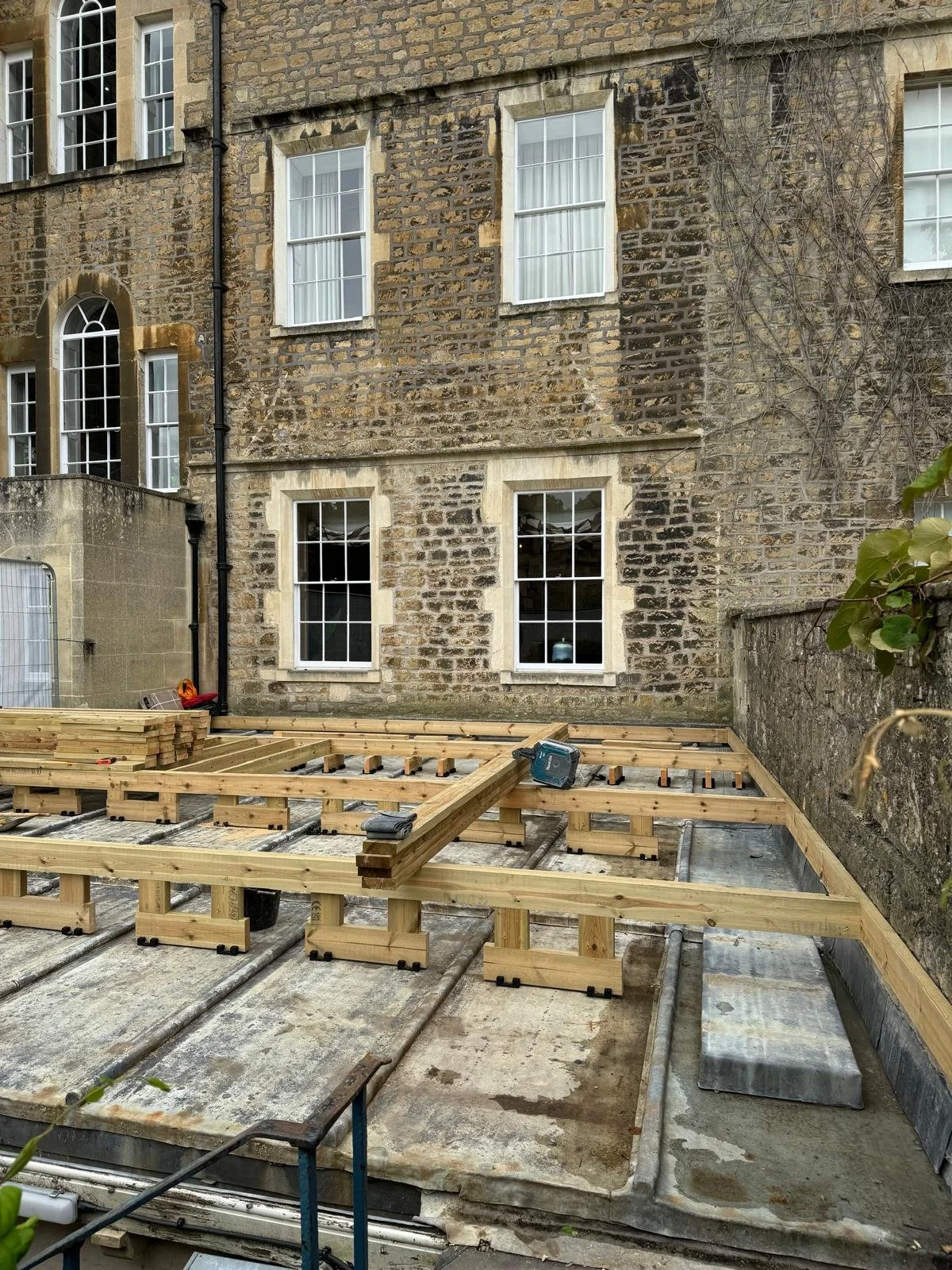 Construction site with wooden framing for a deck or extension at the back of a brick house, with windows and vines on the wall.