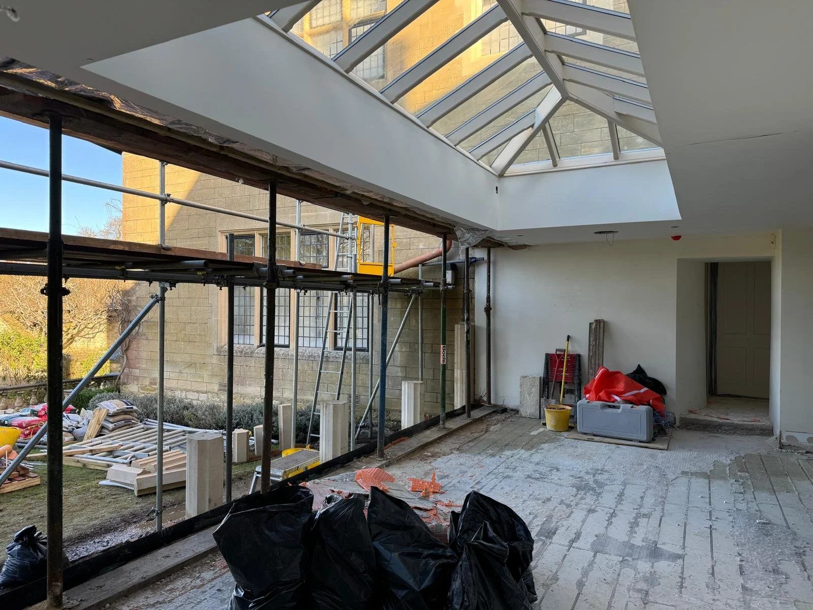 Construction site inside a building with a glass ceiling, scaffolding, and construction materials and tools scattered on the floor.