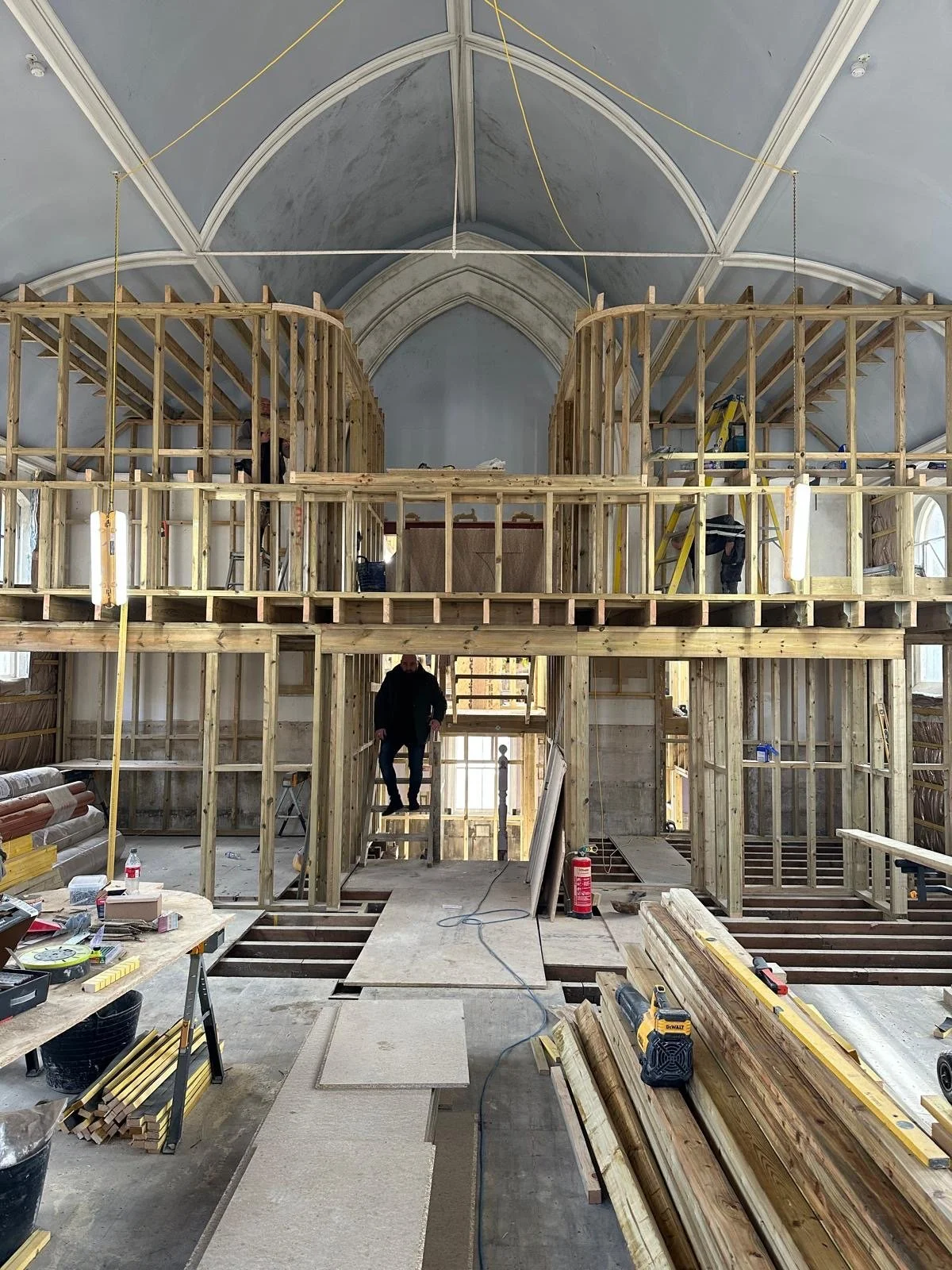 Under construction in Claremont Chapel, showing wooden framing for a balcony or loft area, with workers installing or working on the structure, and construction tools and materials scattered around.