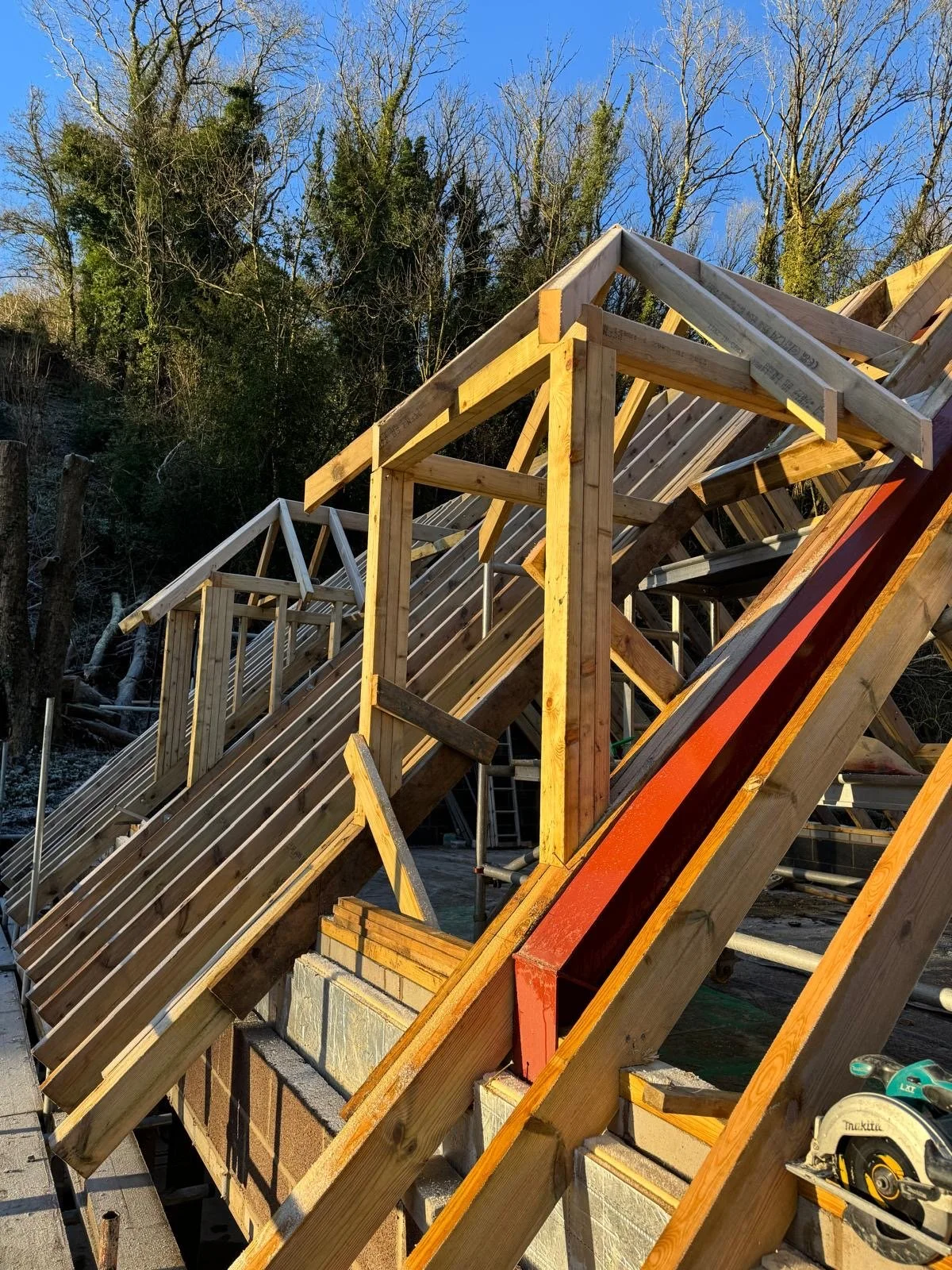 Construction of a wooden roof frame on a building with scaffolding and trees in the background.