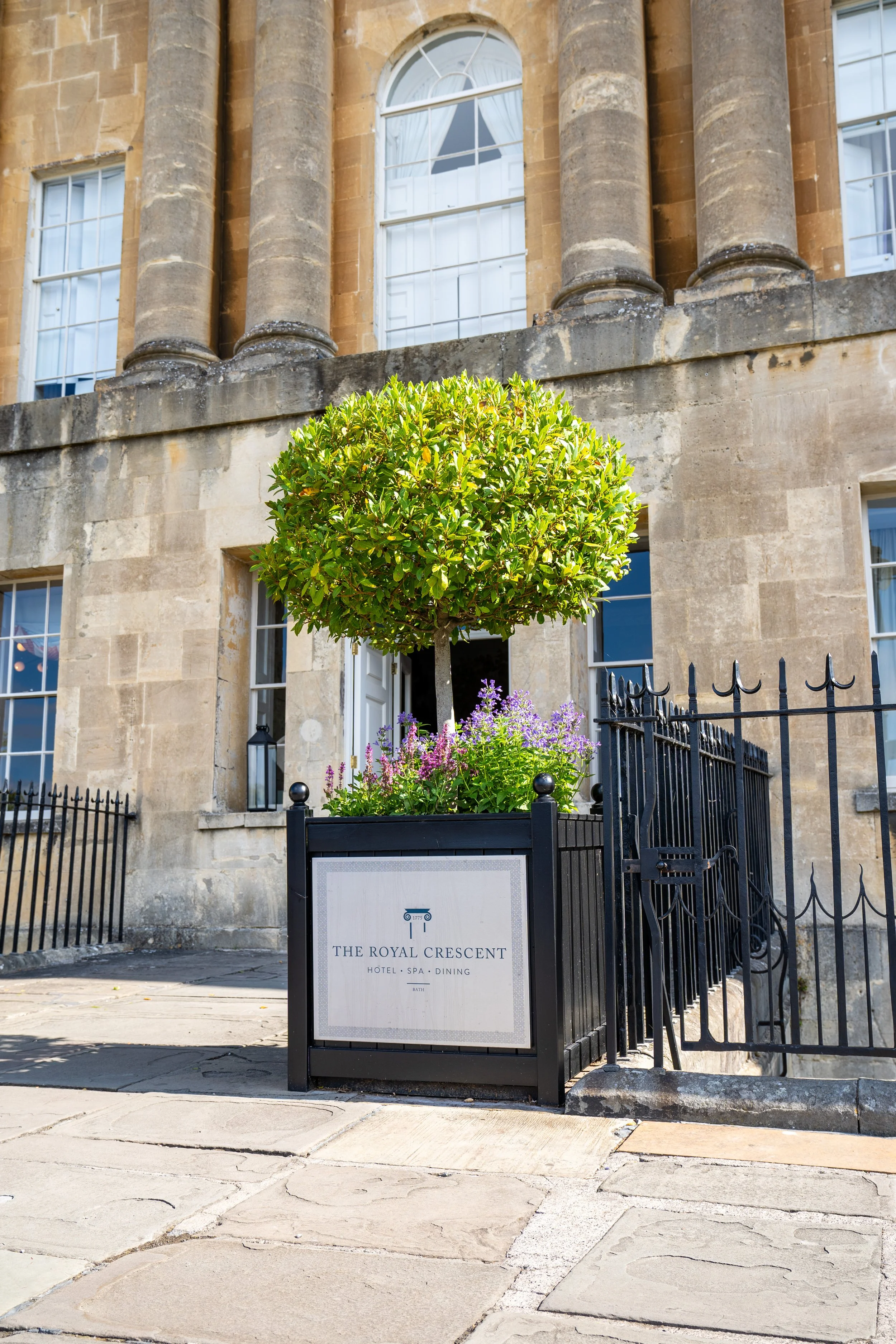 Exterior view of a historic Bath stone building with large windows, a black metal fence, and a sign for The Royal Crescent hotel, spa, and dining.