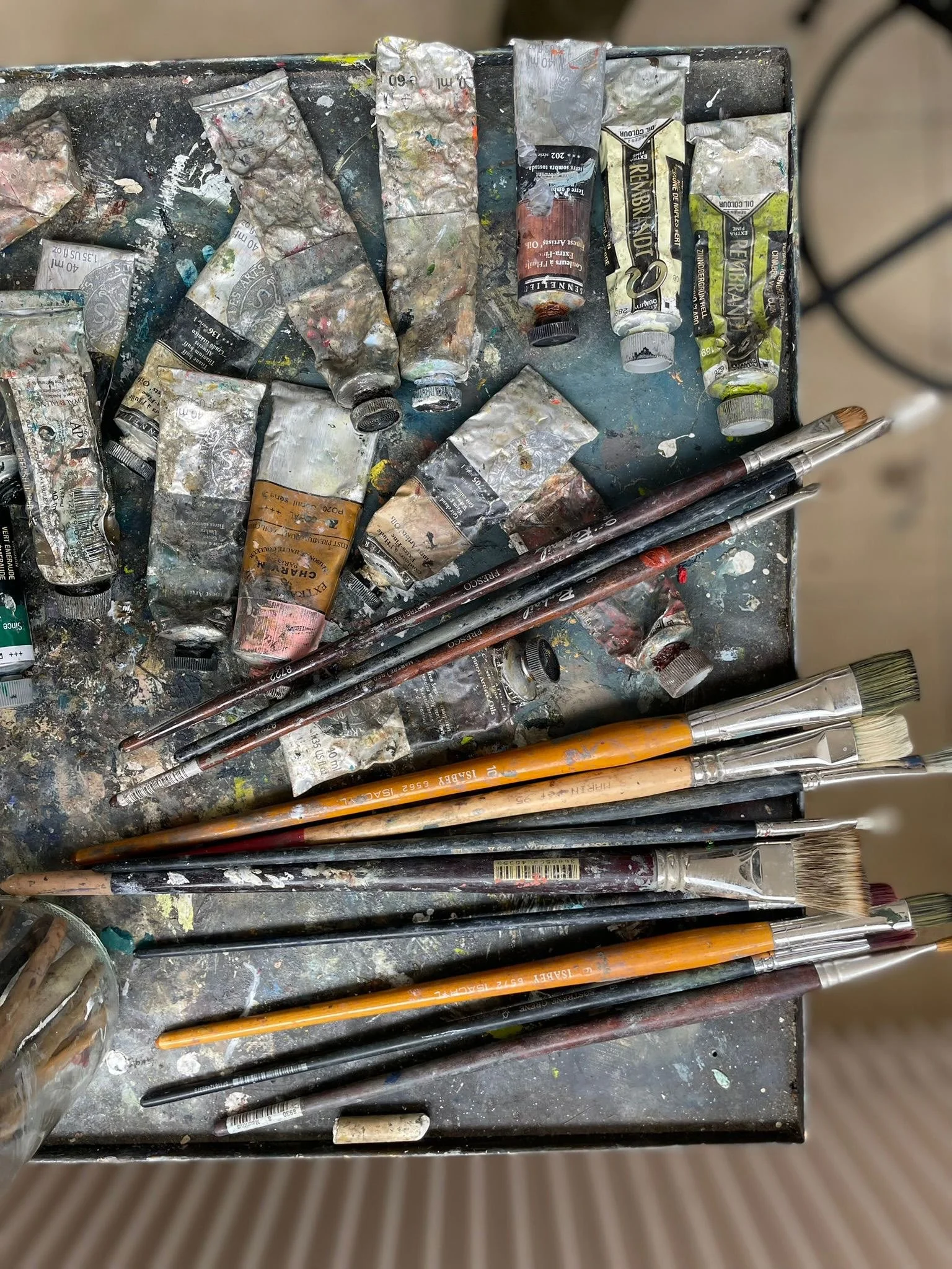 Un plateau contenant divers tubes de peinture, brosses et couteaux de peinture, tous sales et utilisés.