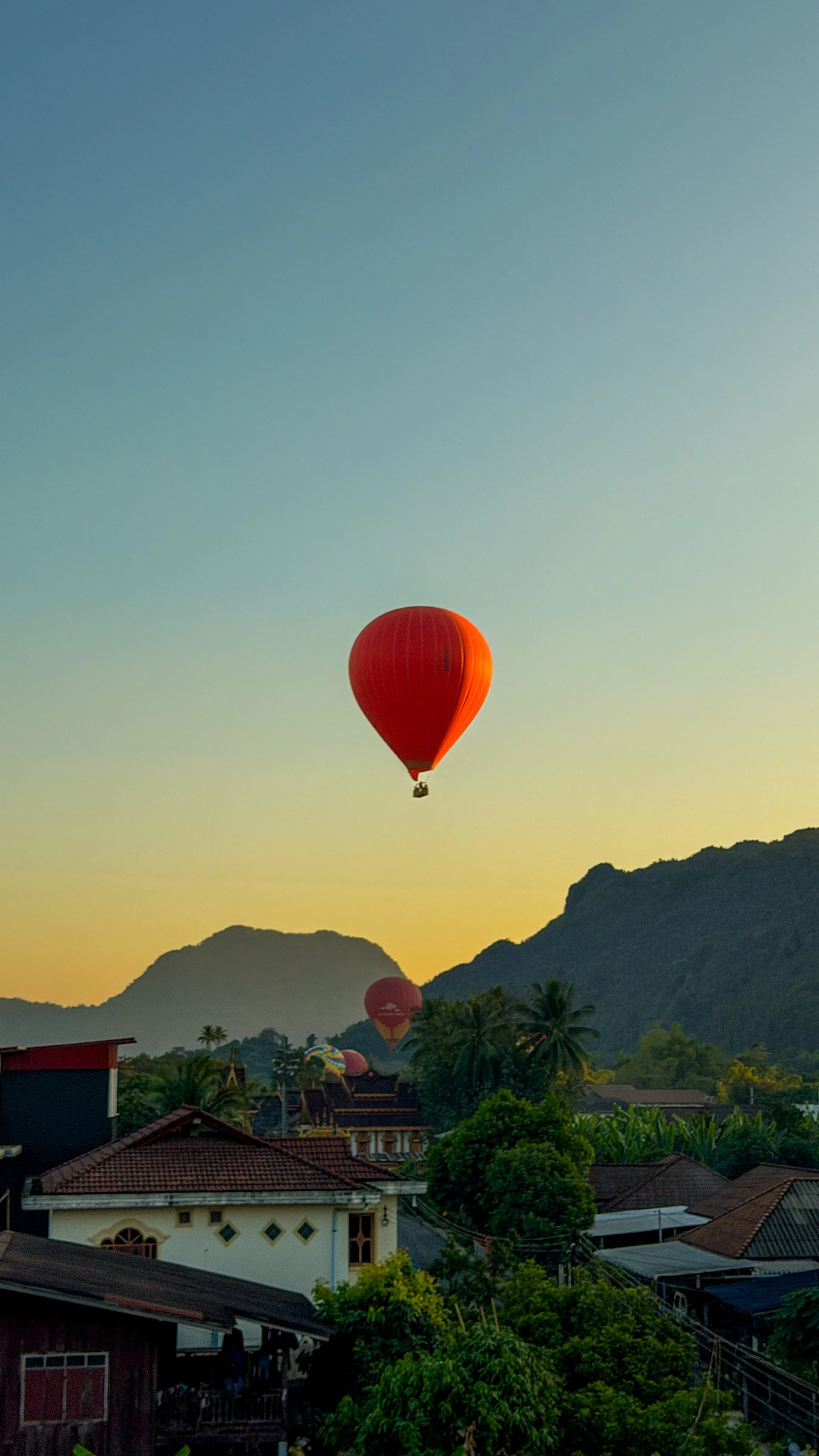 A red hot air balloon floating above a small town with houses, trees, and mountains during sunset. Photo taken by Hailey Tasker, a registered therapist in Ontario, offering remote counselling for young adults