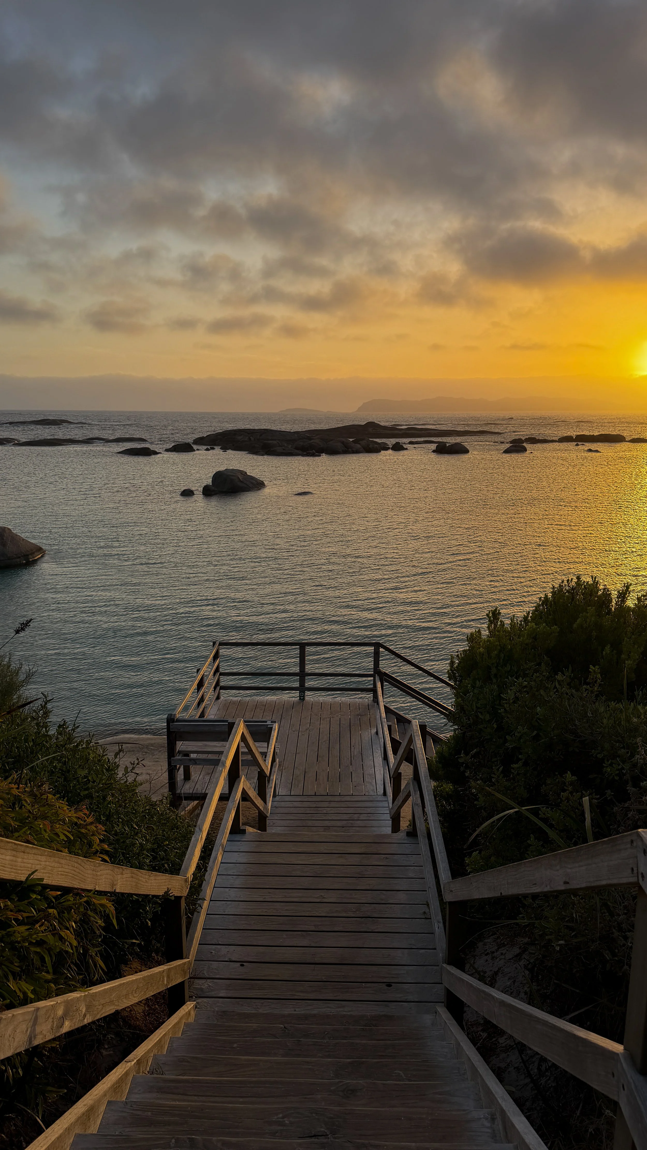 Wooden staircase leading down to the shoreline with water and rocks, during sunset with a cloudy sky. Photo taken by Hailey Tasker, a registered therapist in Ontario, offering remote counselling for young adults.