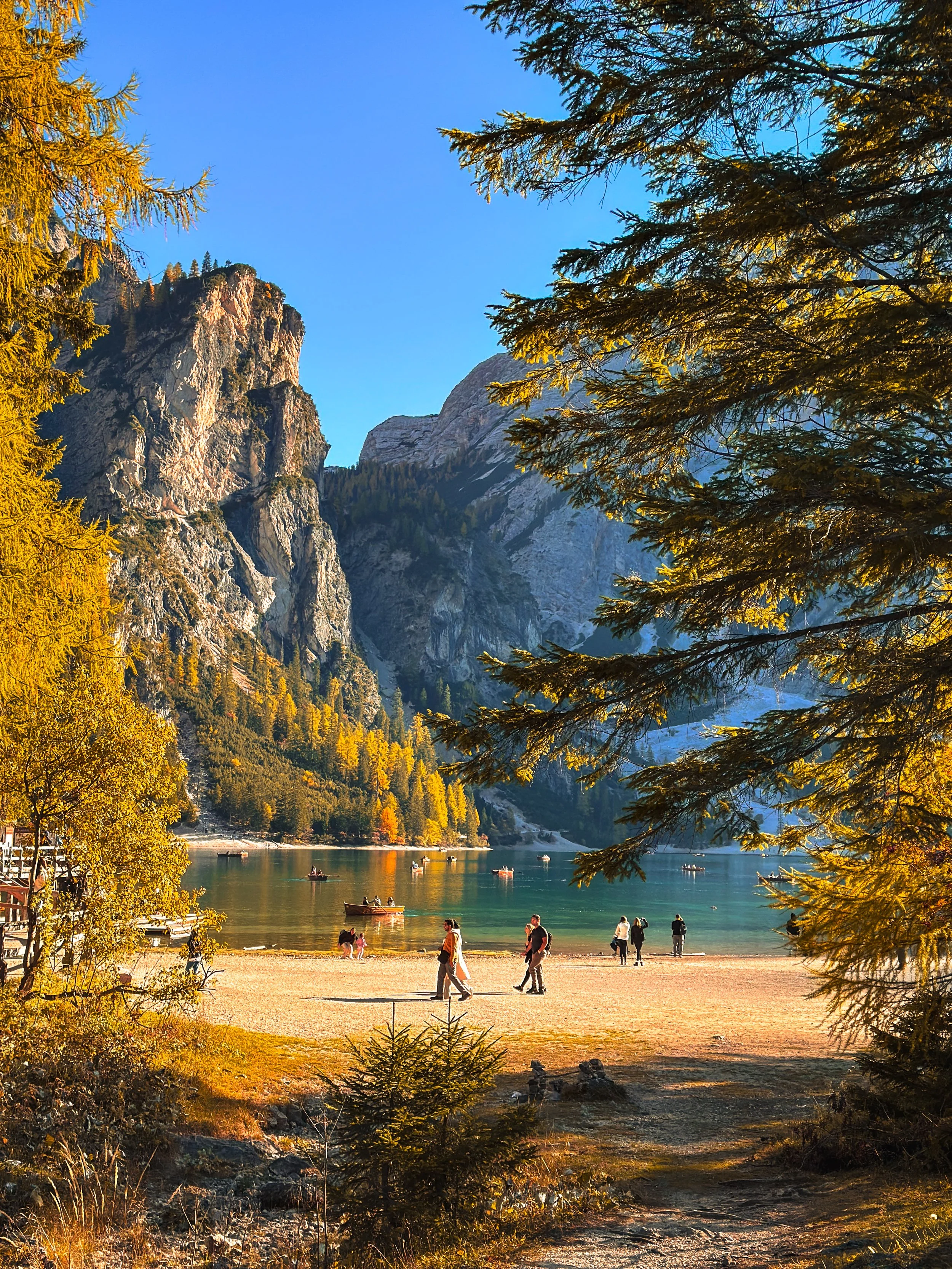 A scenic view of a lake surrounded by mountains and trees, with people enjoying the shoreline and boats on the water during autumn. Photo taken by Hailey Tasker, a registered therapist in Ontario, offering remote counselling for young adults