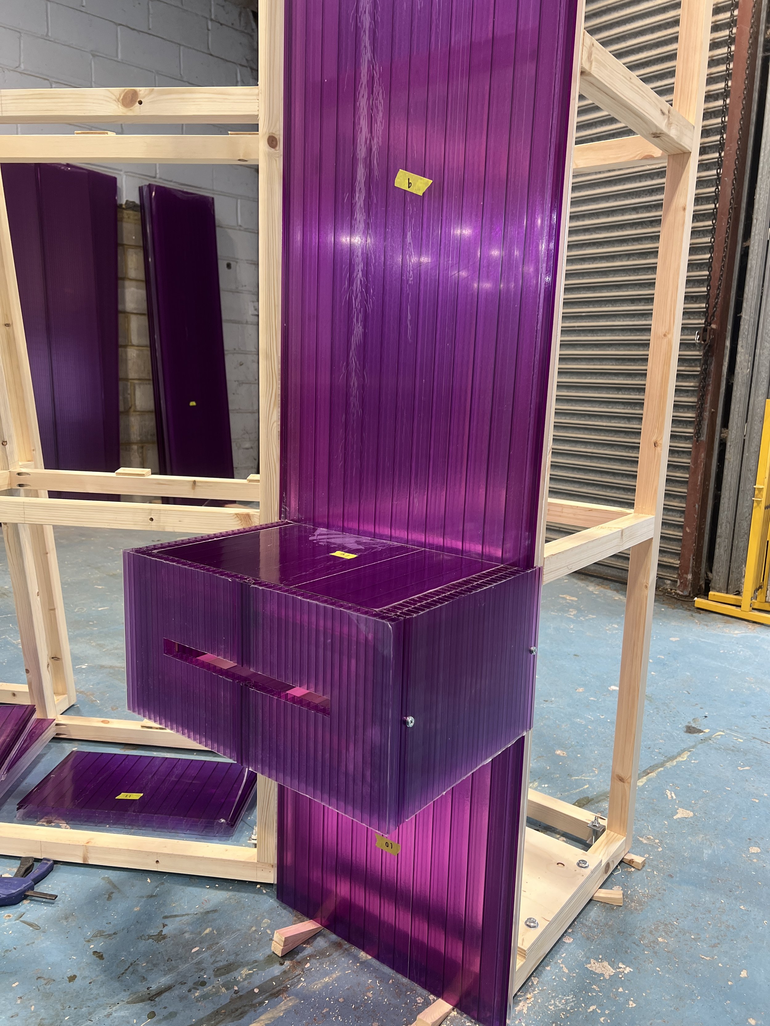 Purple glass panels assembled on a wooden frame in an indoor workspace.