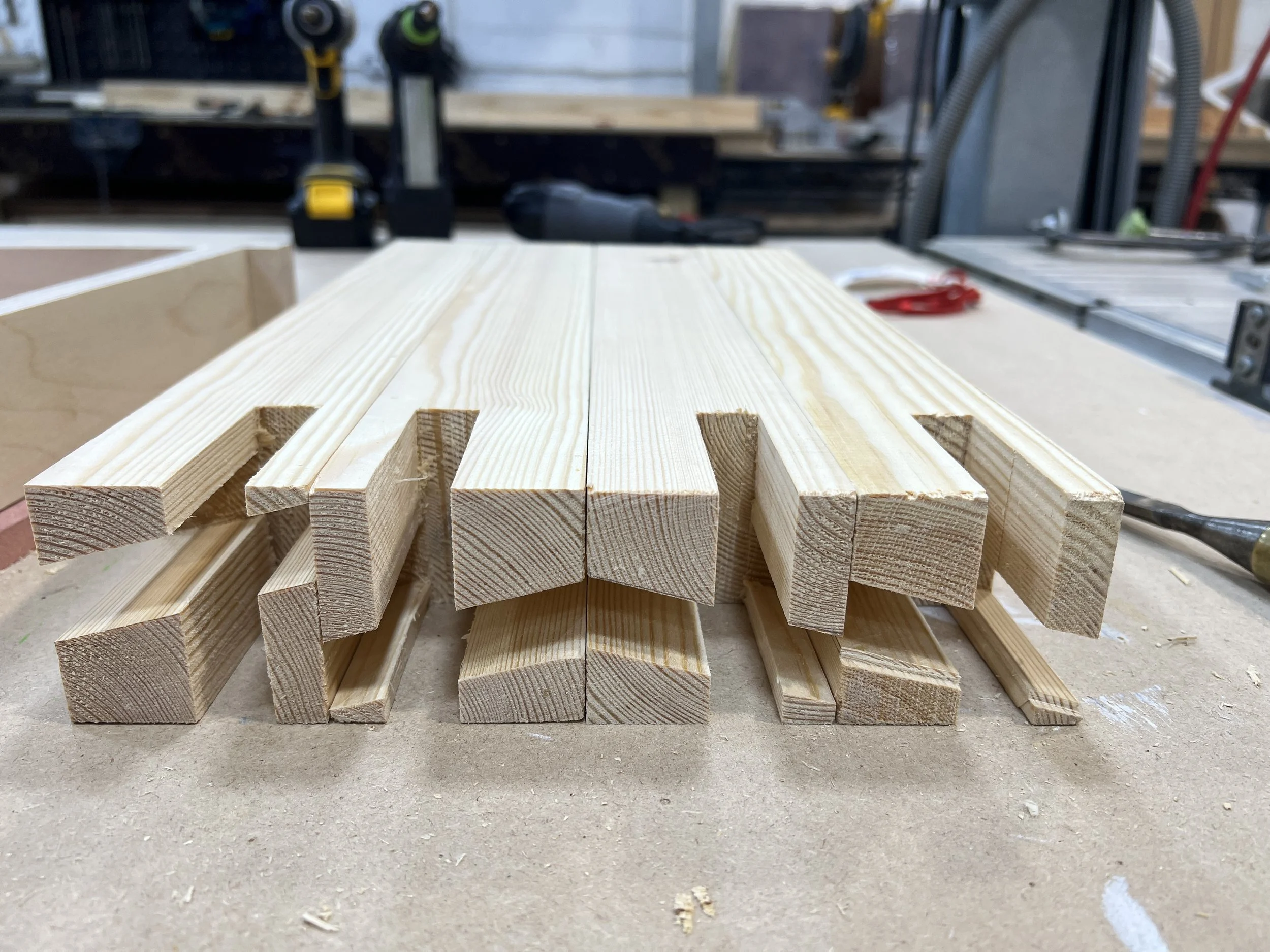 Close-up of a stack of wooden slats with a workshop in the background, power tools, and workbench.