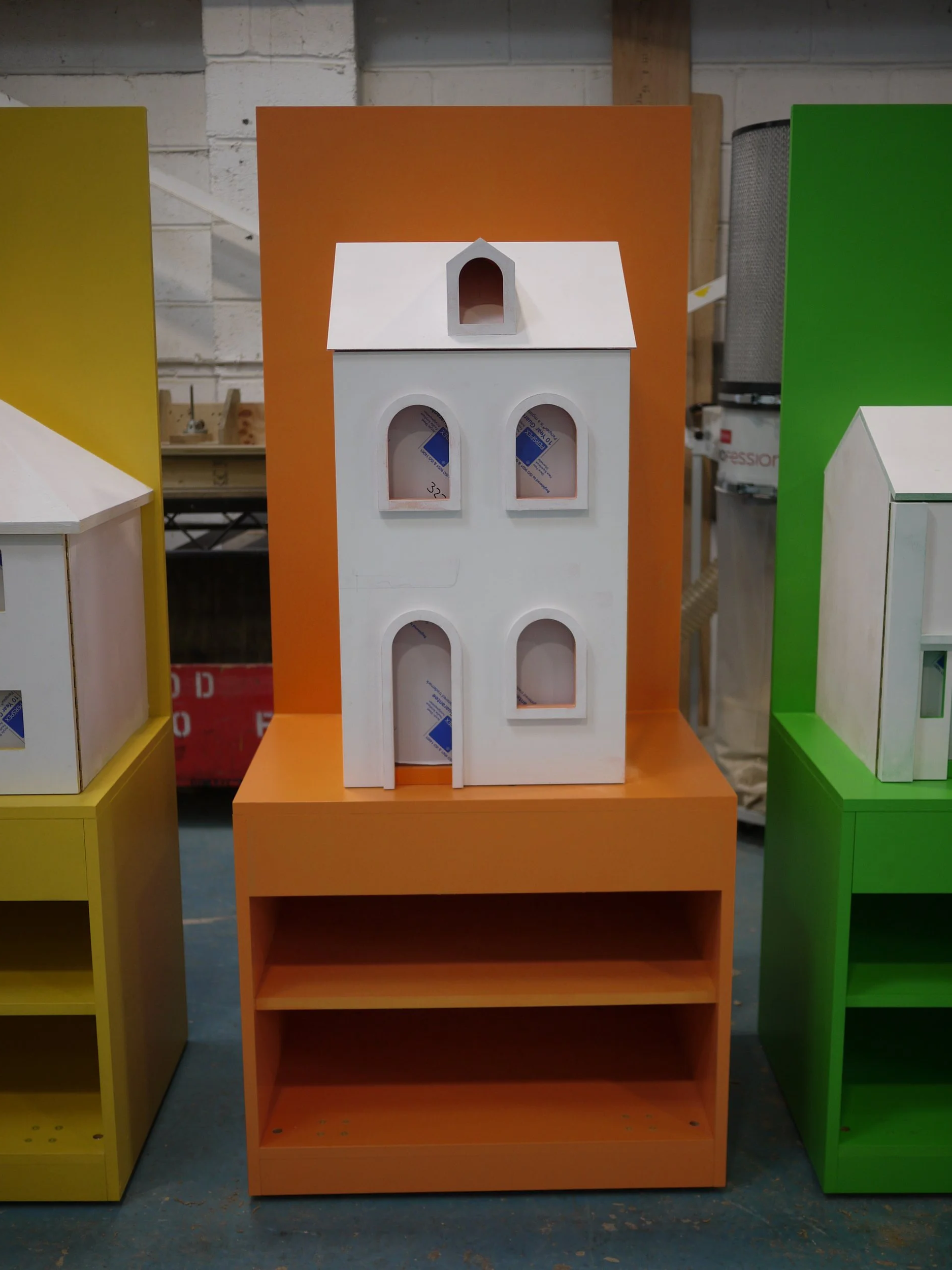 Colorful display shelves in yellow, orange, and green with a white miniature house on the orange shelf.