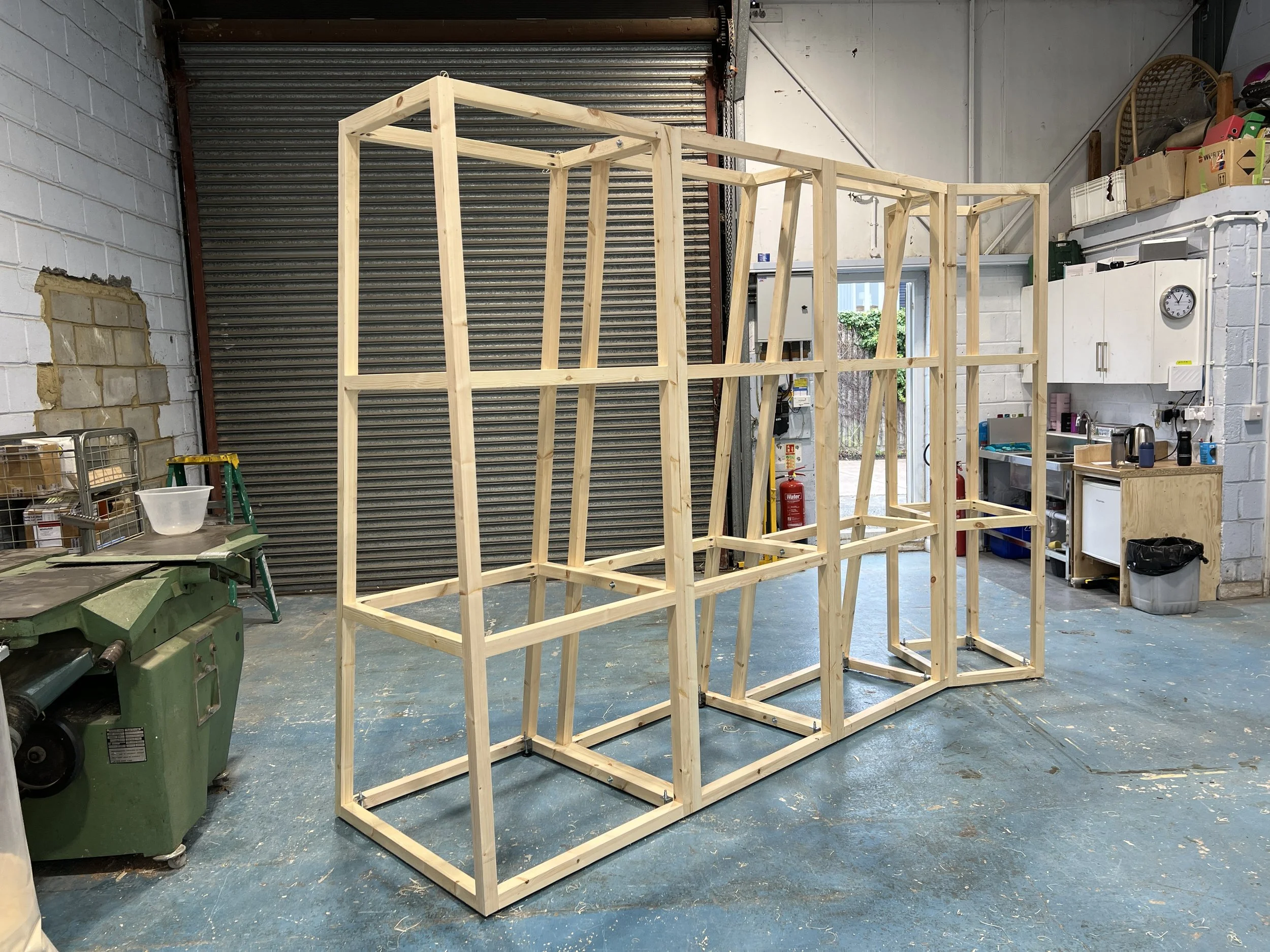 Wooden frame structure in a workshop or warehouse, with various tools and storage on the side.