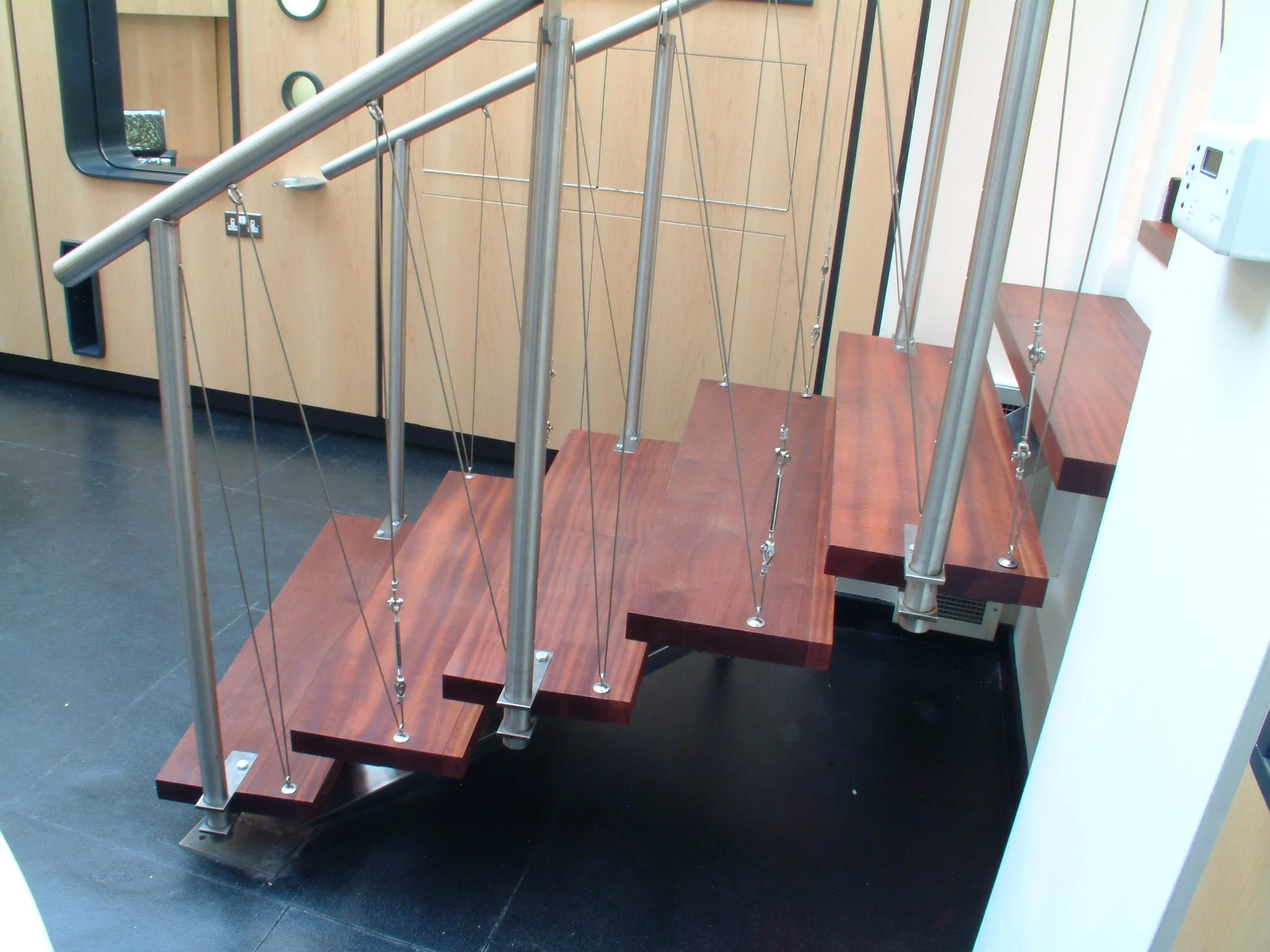 A staircase with wooden steps and metal railings in an indoor setting, adjacent to a wooden wall with a mirror and a fire alarm.