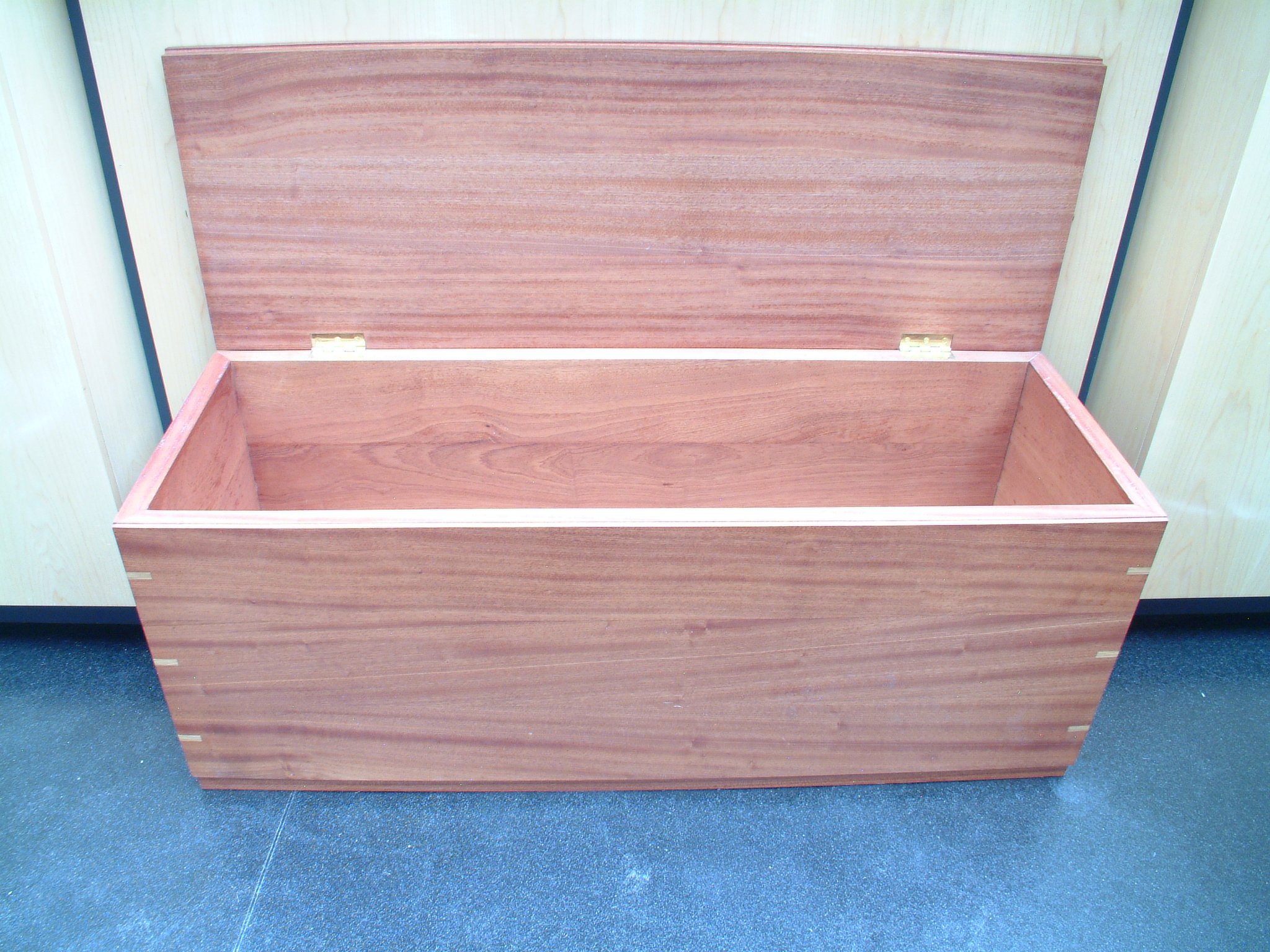 Empty wooden storage chest with a hinged lid in a room with blue carpeted floor.