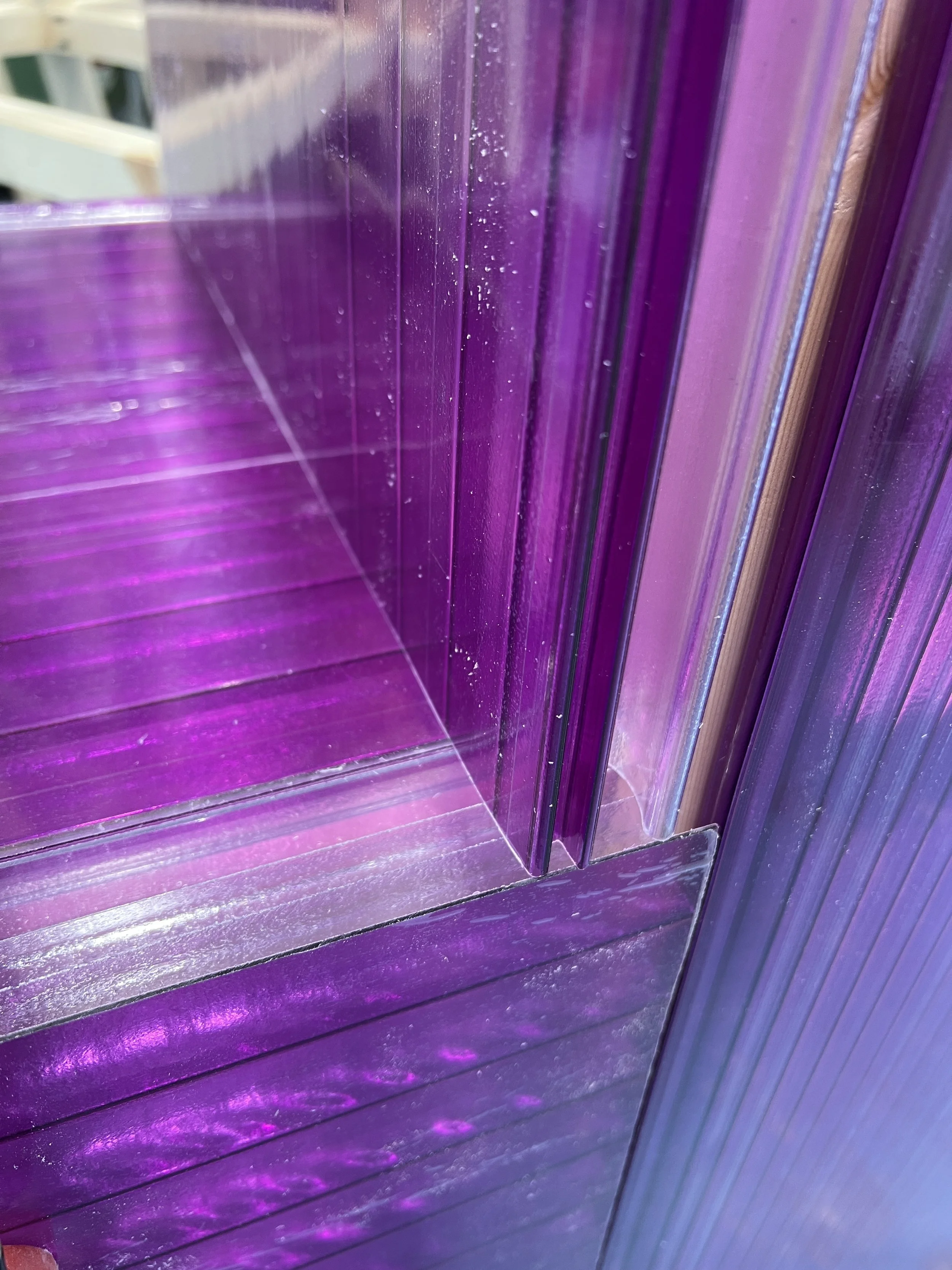 Close-up of a purple, glossy, reflective display case or shelf with multiple layers of purple-tinted glass or acrylic, creating a vibrant, colorful effect.