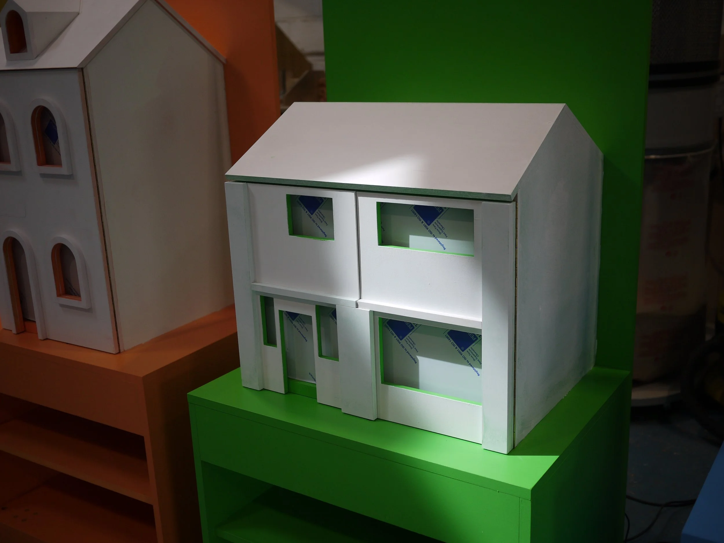 Multiple miniature display cabinets on green, orange, and white shelves, each with glass front panels and sticker sheets inside, set against colorful backdrops.
