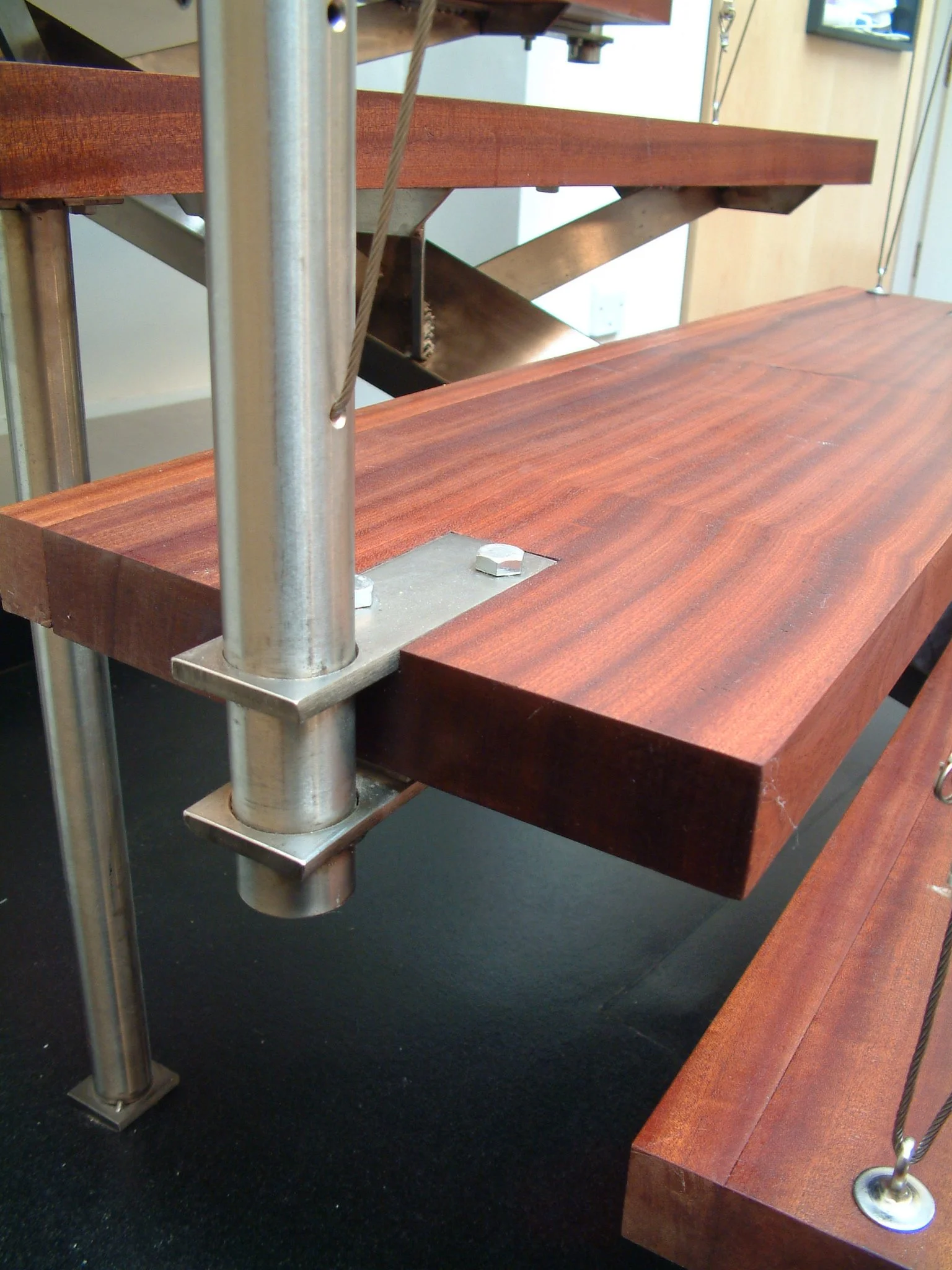 Close-up of a wooden table with metal support structures in a room with a black floor. Part of a mirror and electrical outlet are visible in the background.