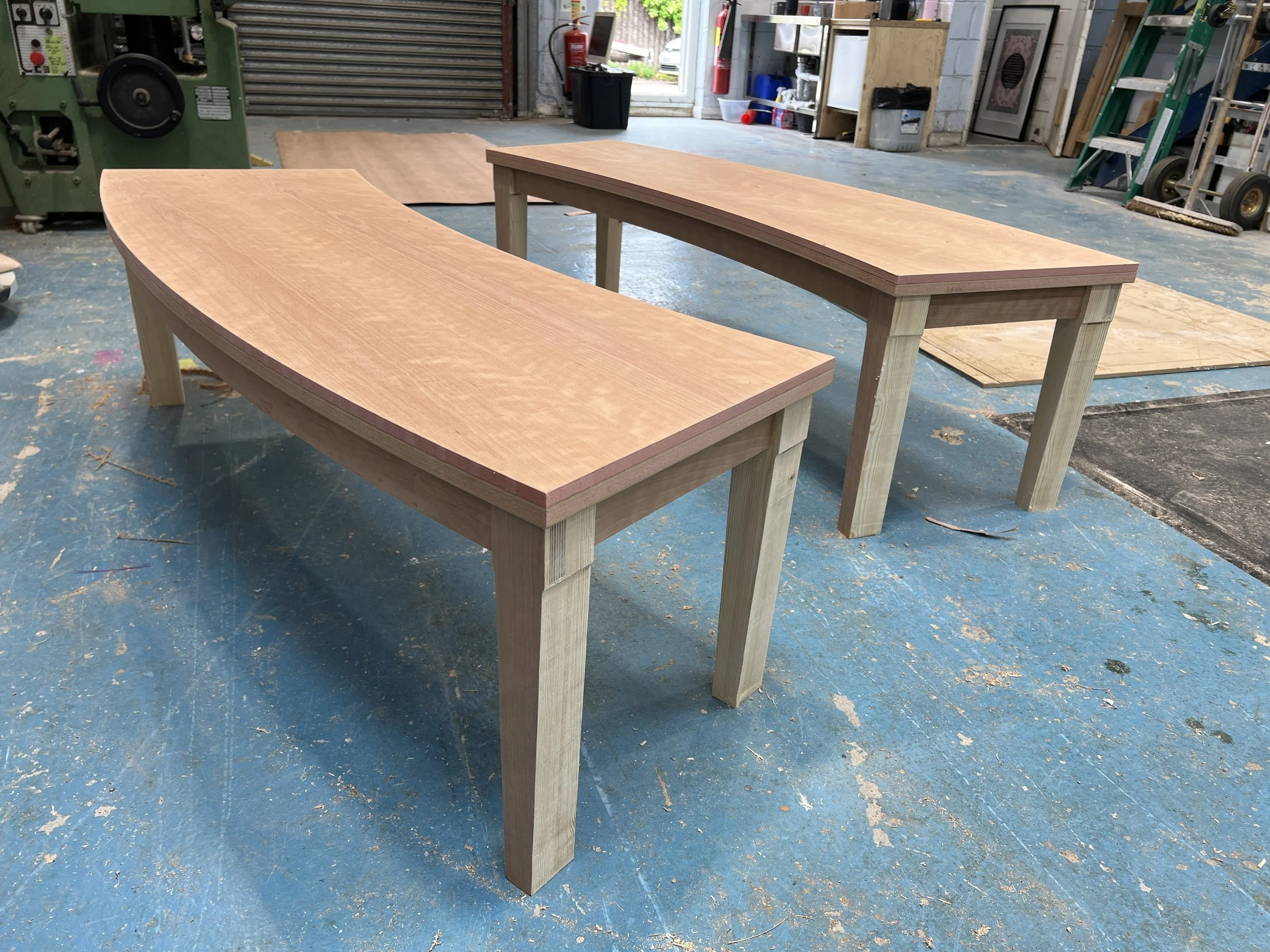 Unfinished wooden table with a curved top in a workshop.