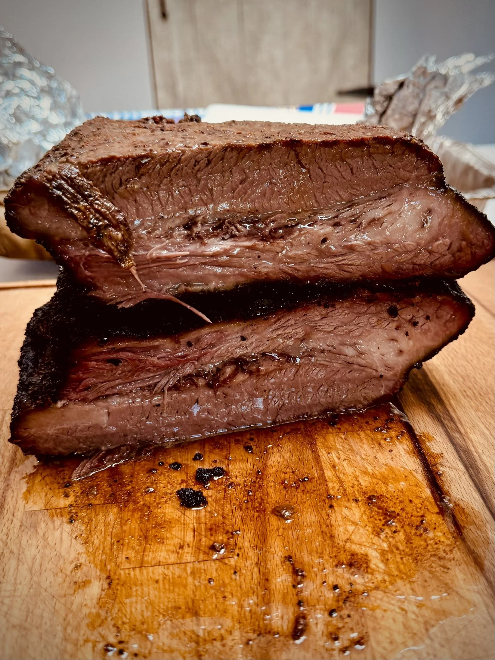A large piece of cooked meat on a wooden cutting board, with juices and some charred areas visible.