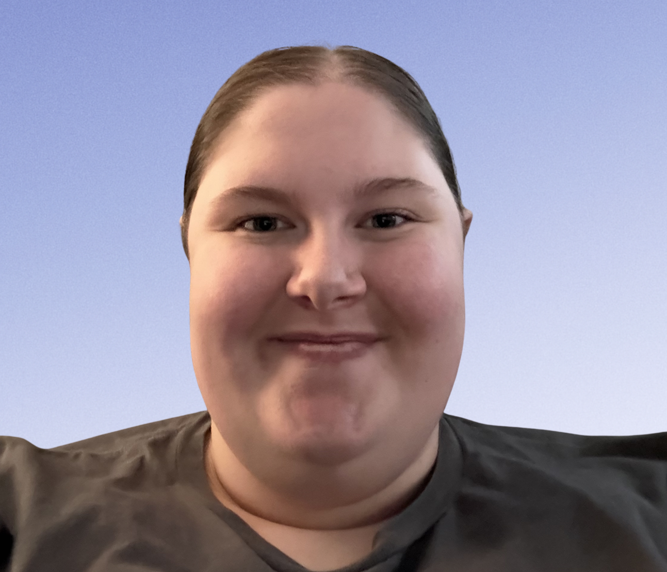 A person with short brown hair, smiling in front of a light blue background, wearing a dark shirt.