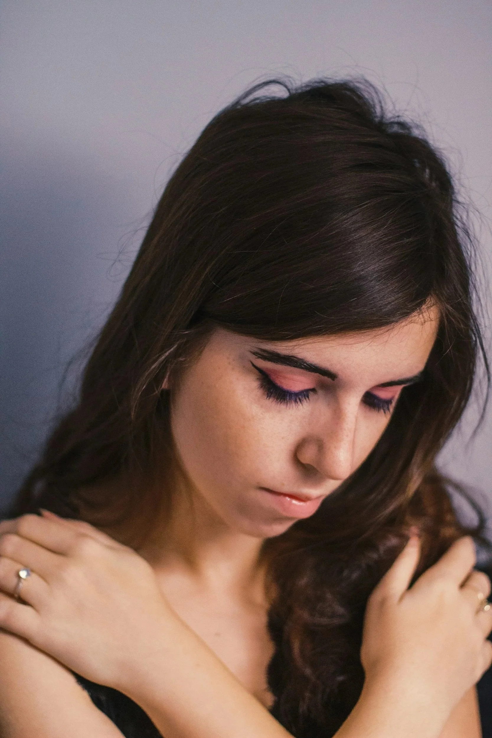 A woman with brown hair, eyes closed, and makeup including eyeliner and mascara, resting her head on her hand.