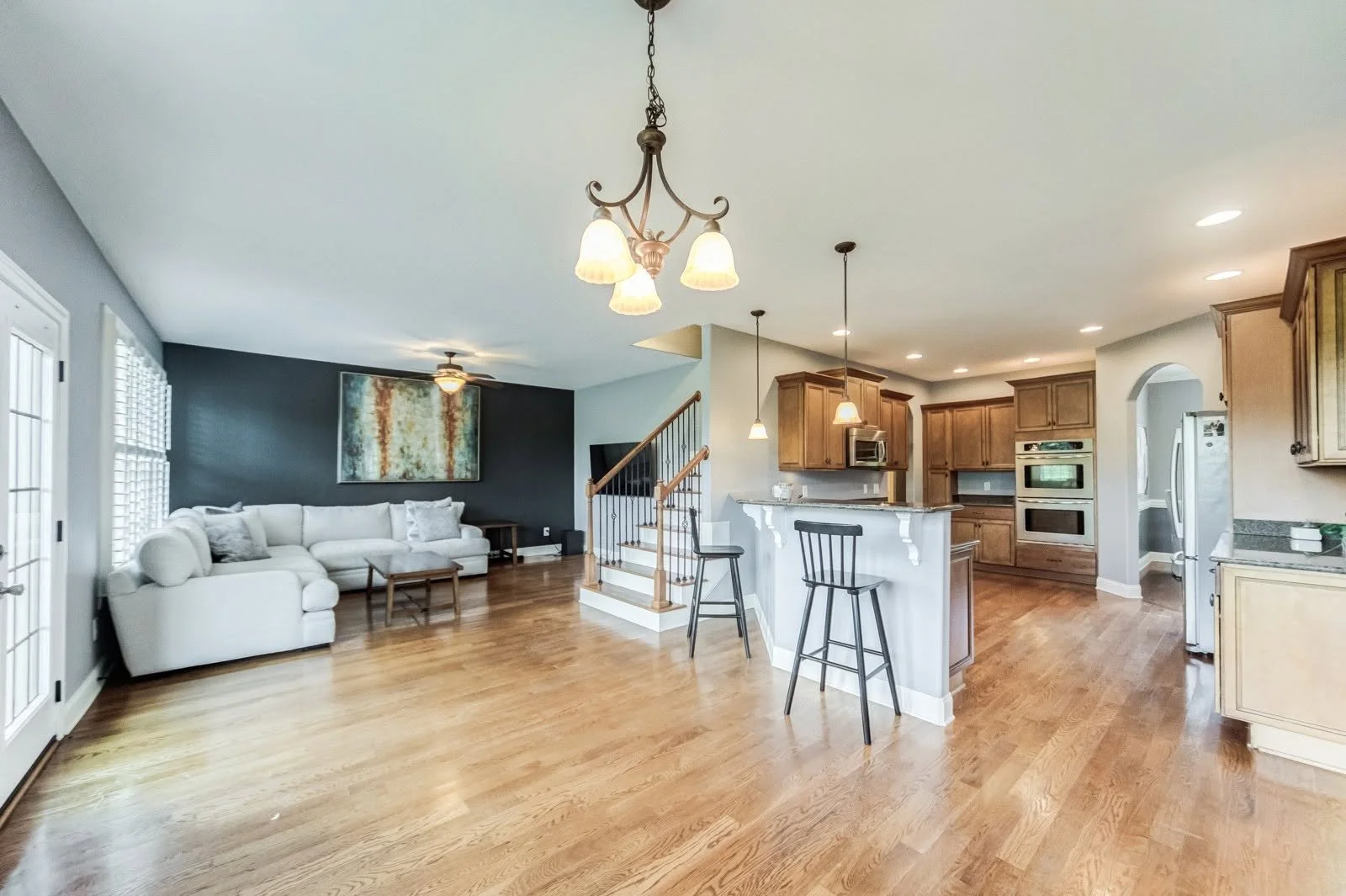 Open-concept living room and kitchen with hardwood floors, white sofa, dark accent wall, and wooden cabinetry.