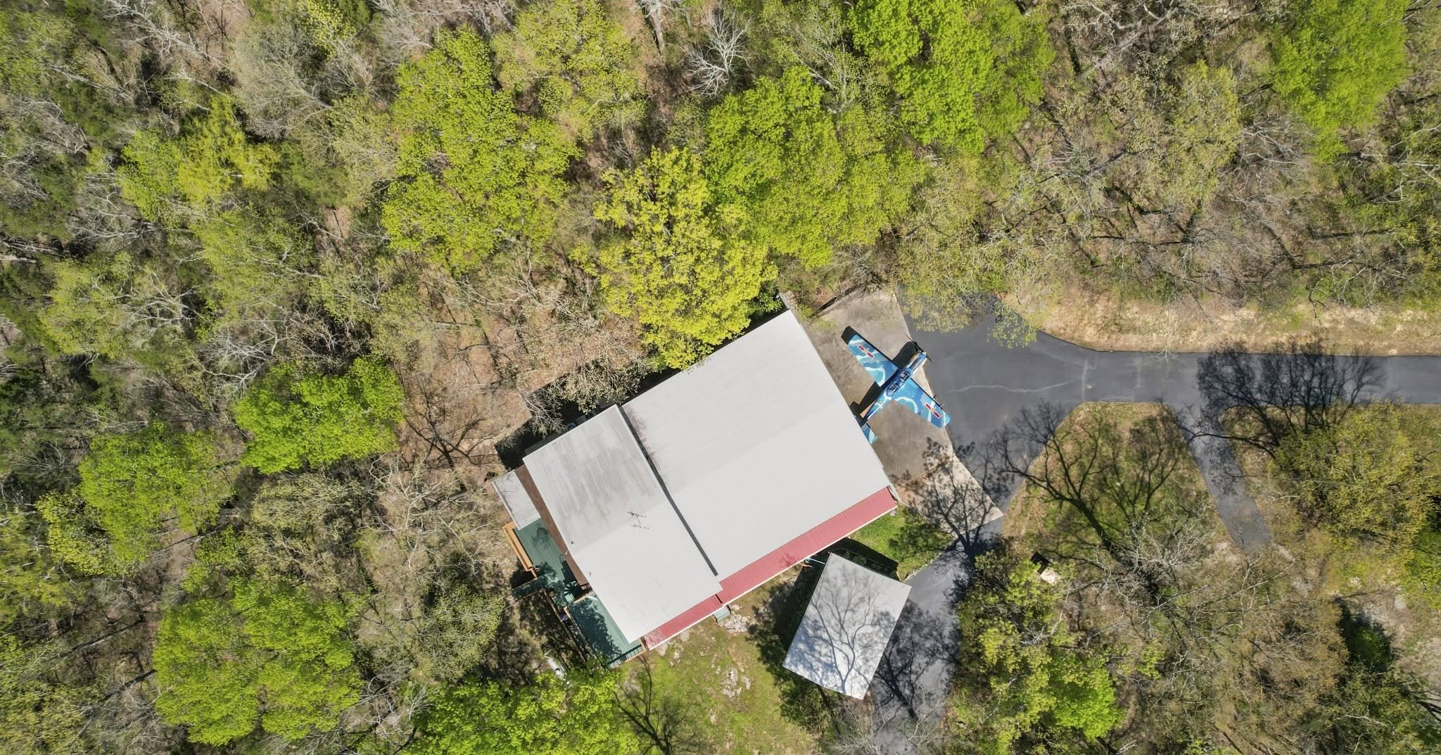 Aerial view of a building surrounded by a dense forest with a narrow driveway leading to the building.