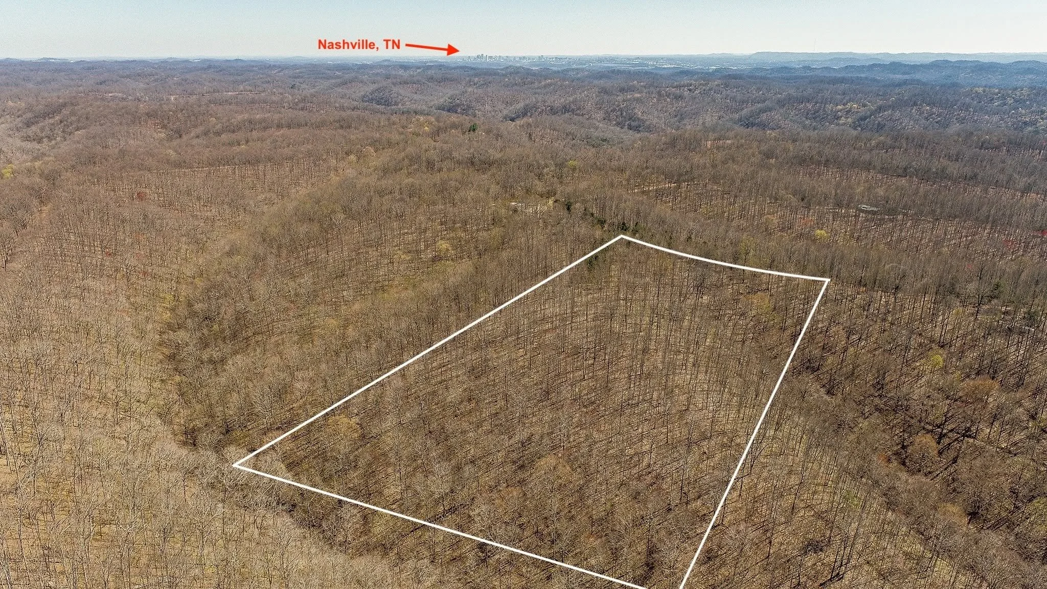 Aerial view of a forested hilly area with a marked rectangular plot outlined in white, with a city skyline labeled Nashville, TN visible in the distance.