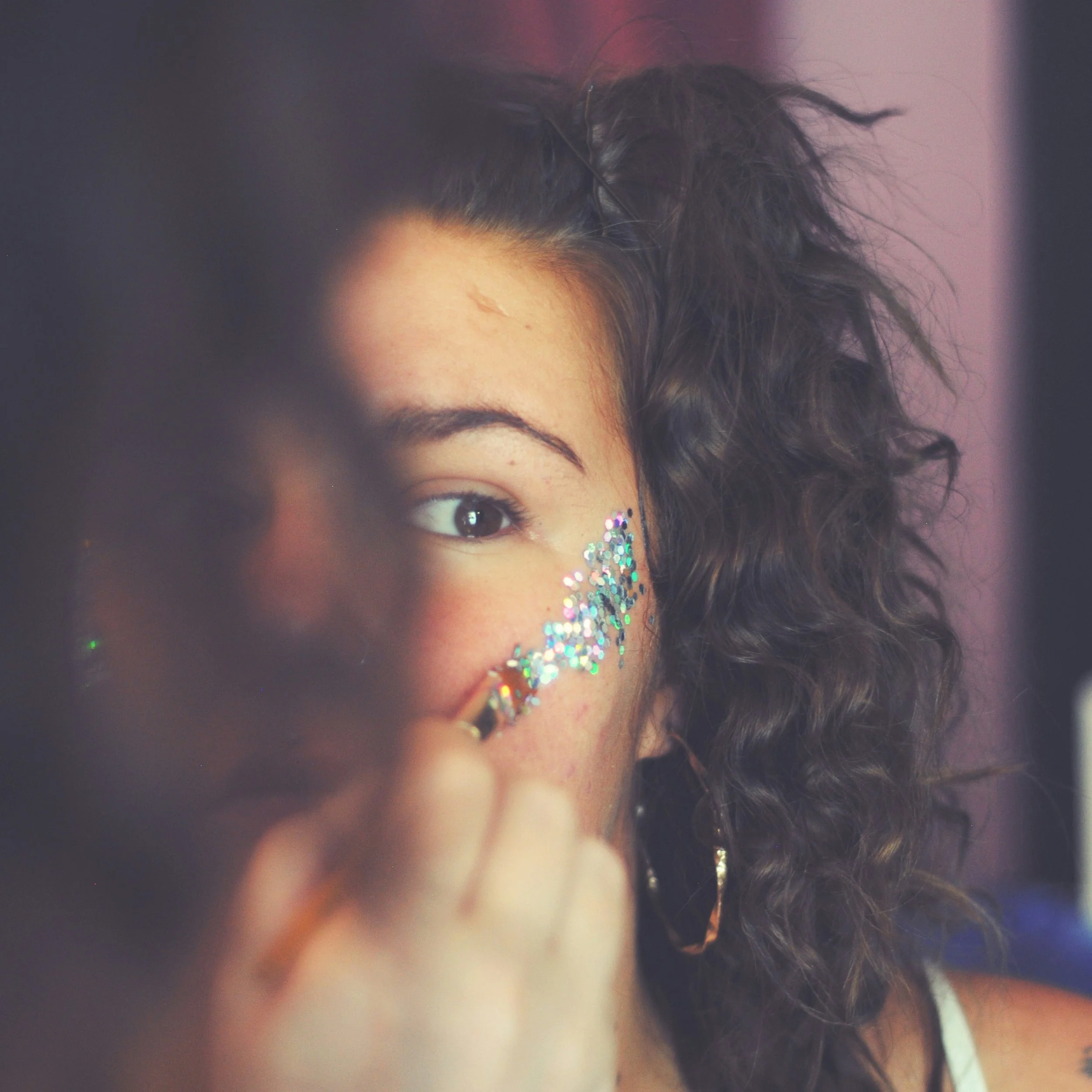 Close-up of a woman's face, with focus on her eye and eyebrow, decorated with colorful glitter.