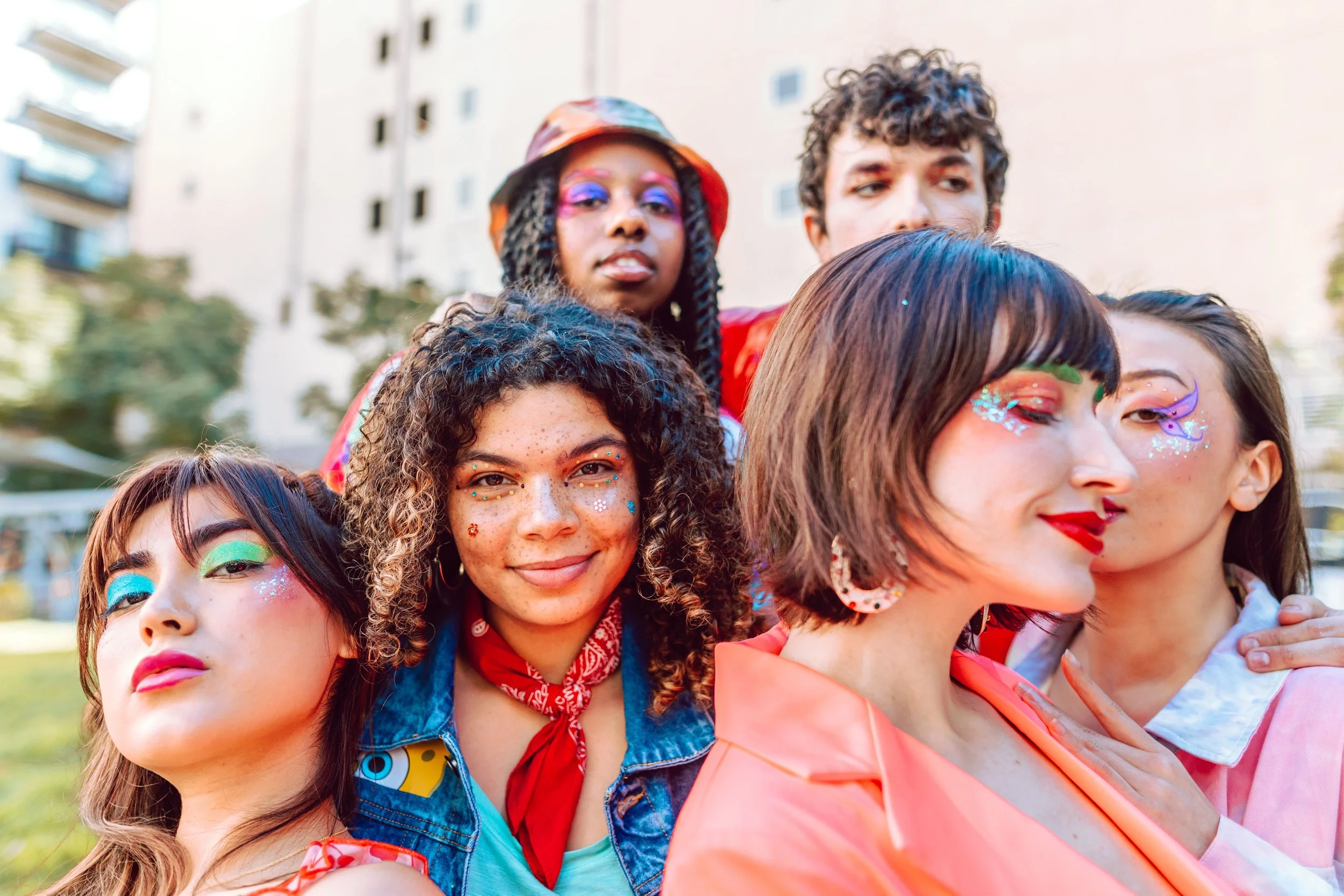 A diverse group of young women with colorful face makeup and accessories, smiling together outdoors.